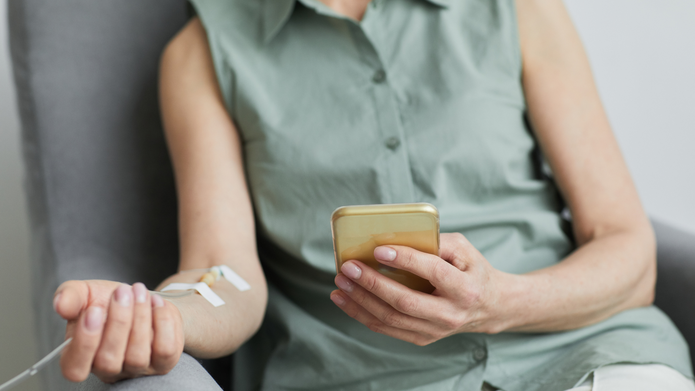 Woman receiving an IV drip in her arm while relaxing in a chair holding her phone