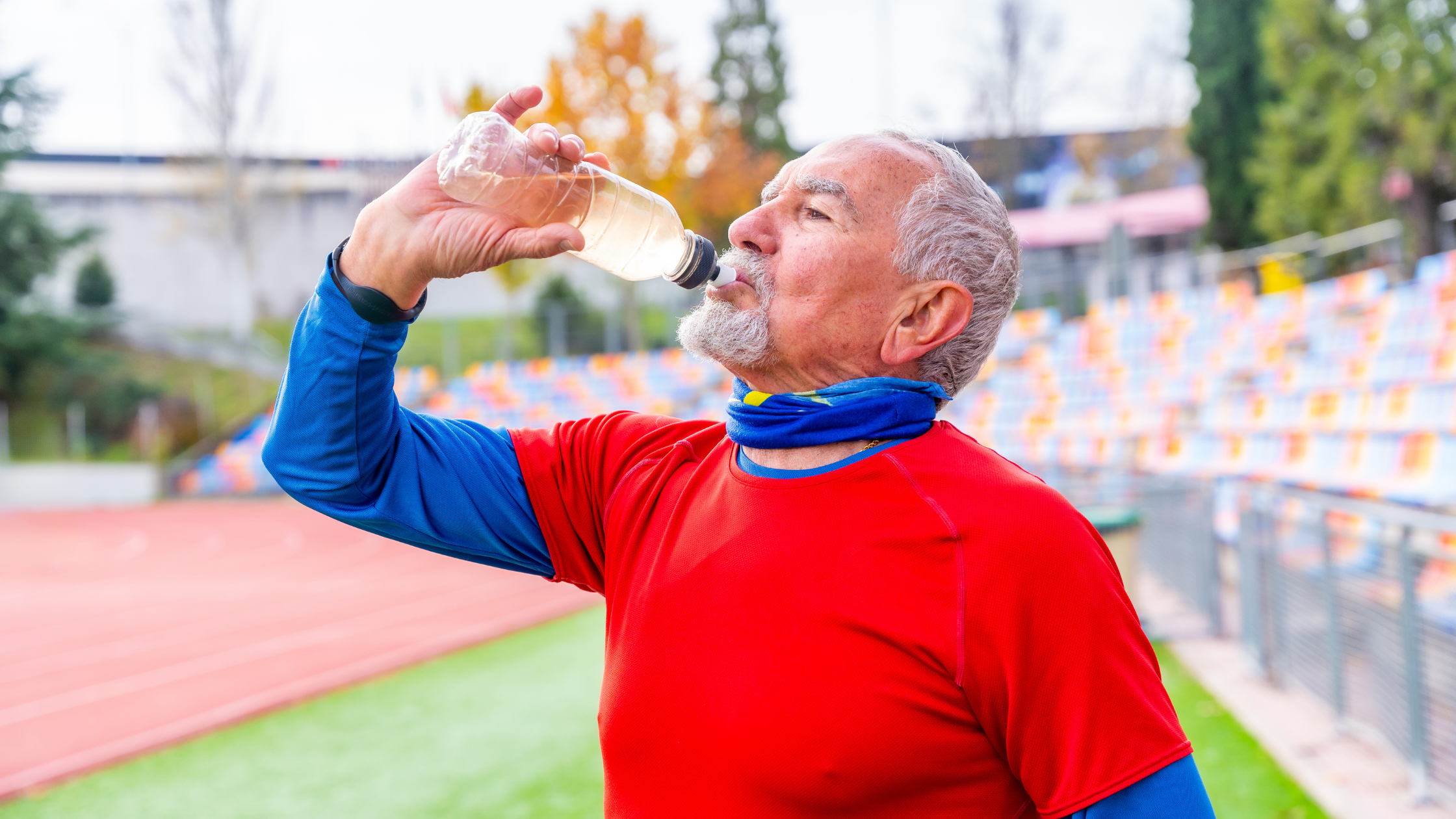 Active older man drinking water from a bottle at an outdoor running track