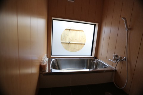Bathroom with warm wood paneling, stainless steel soaking tub, and circular bamboo window shade