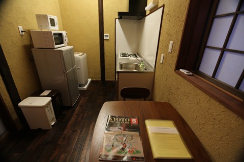 Compact kitchen with refrigerator, microwave, sink unit, and low wooden table with Kyoto guidebook