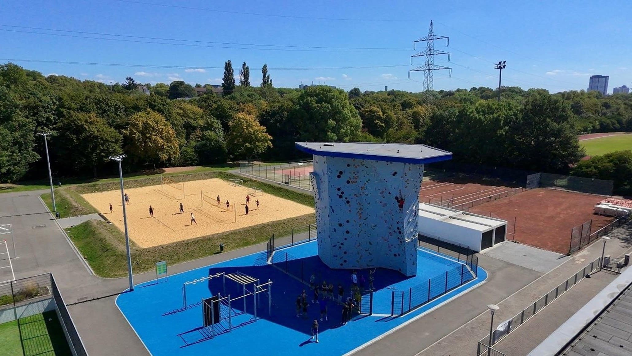Luftaufnahme des Sportcampus der Universität Duisburg-Essen: blauer Calisthenics-Bereich mit Kletterwand, Beachvolleyballfeld und Tennisplatz