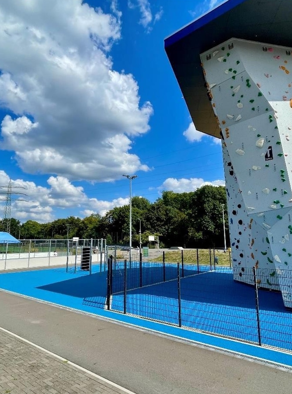 Nahaufnahme der 12 Meter hohen Kletterwand des Sportcampus mit bunten Griffen und blauem Untergrund