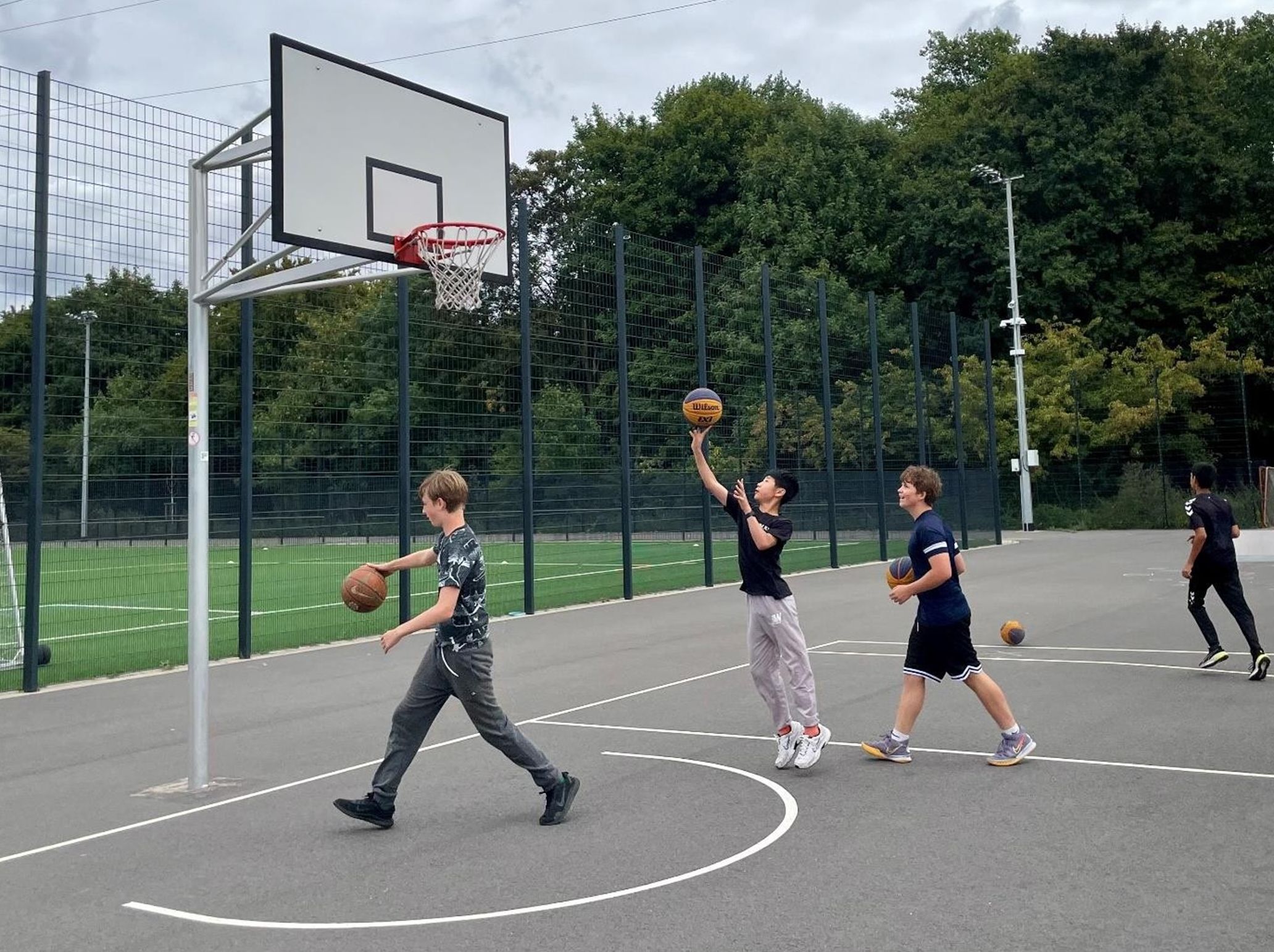 Vier Jugendliche spielen Basketball auf einem Außenplatz mit Basketballkorb