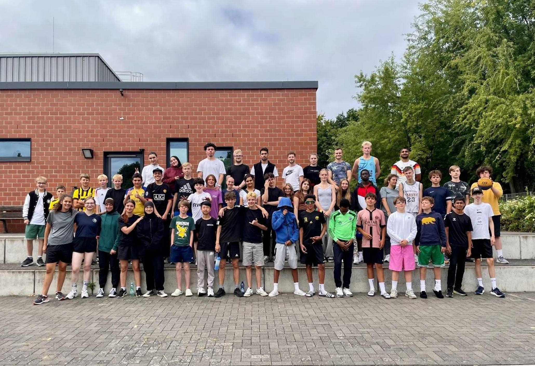 Großes Gruppenfoto: rund 50 Jugendliche und Coaches stehen vor einem Backsteingebäude auf dem Sportcampus