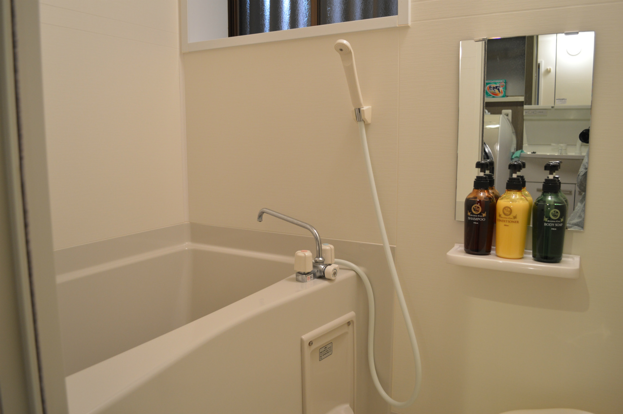 Clean modern Japanese bathroom with white tiles, bathtub, shower, and premium amenities