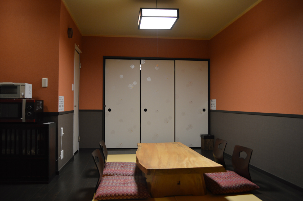 Japanese dining room with terracotta walls, natural wood chabudai low table, patterned floor cushions, and fusuma sliding doors