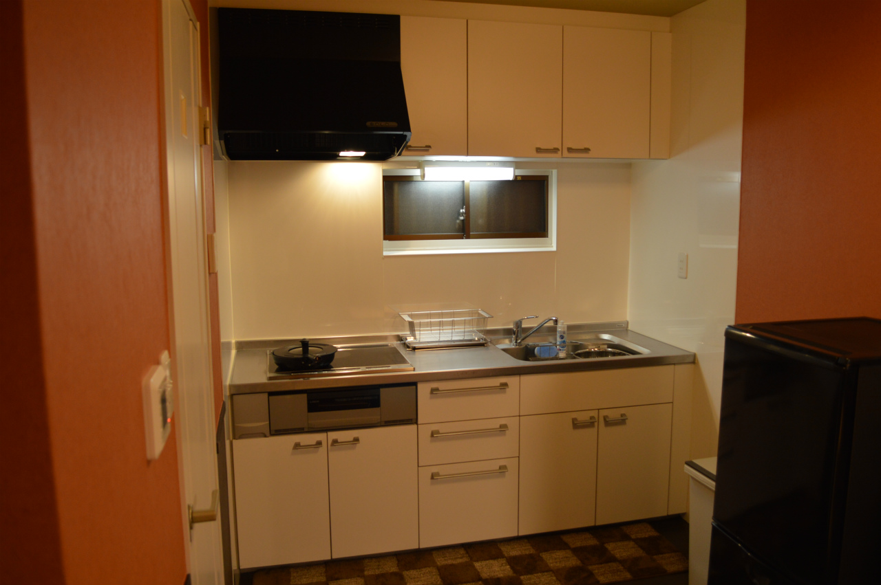 Modern kitchen with cream cabinets, stainless steel countertops, gas cooktop, and terracotta accent walls