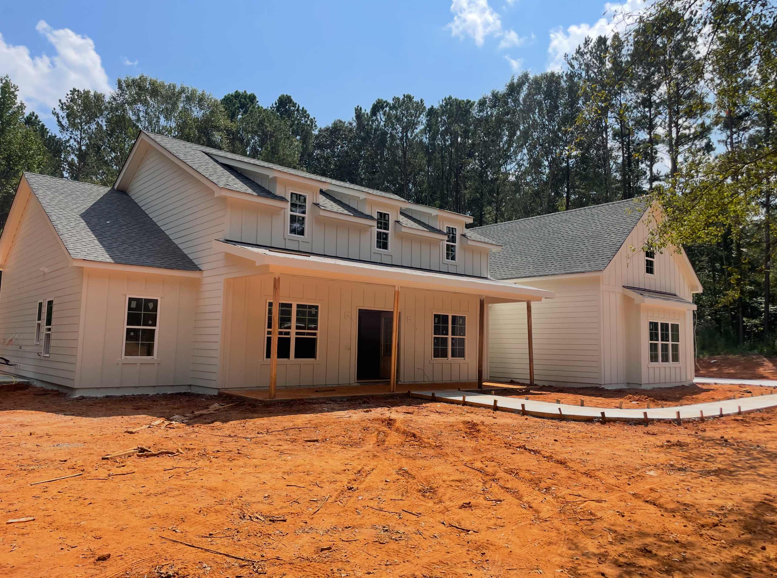 Newly built white board-and-batten custom farmhouse with a covered porch on a cleared homesite