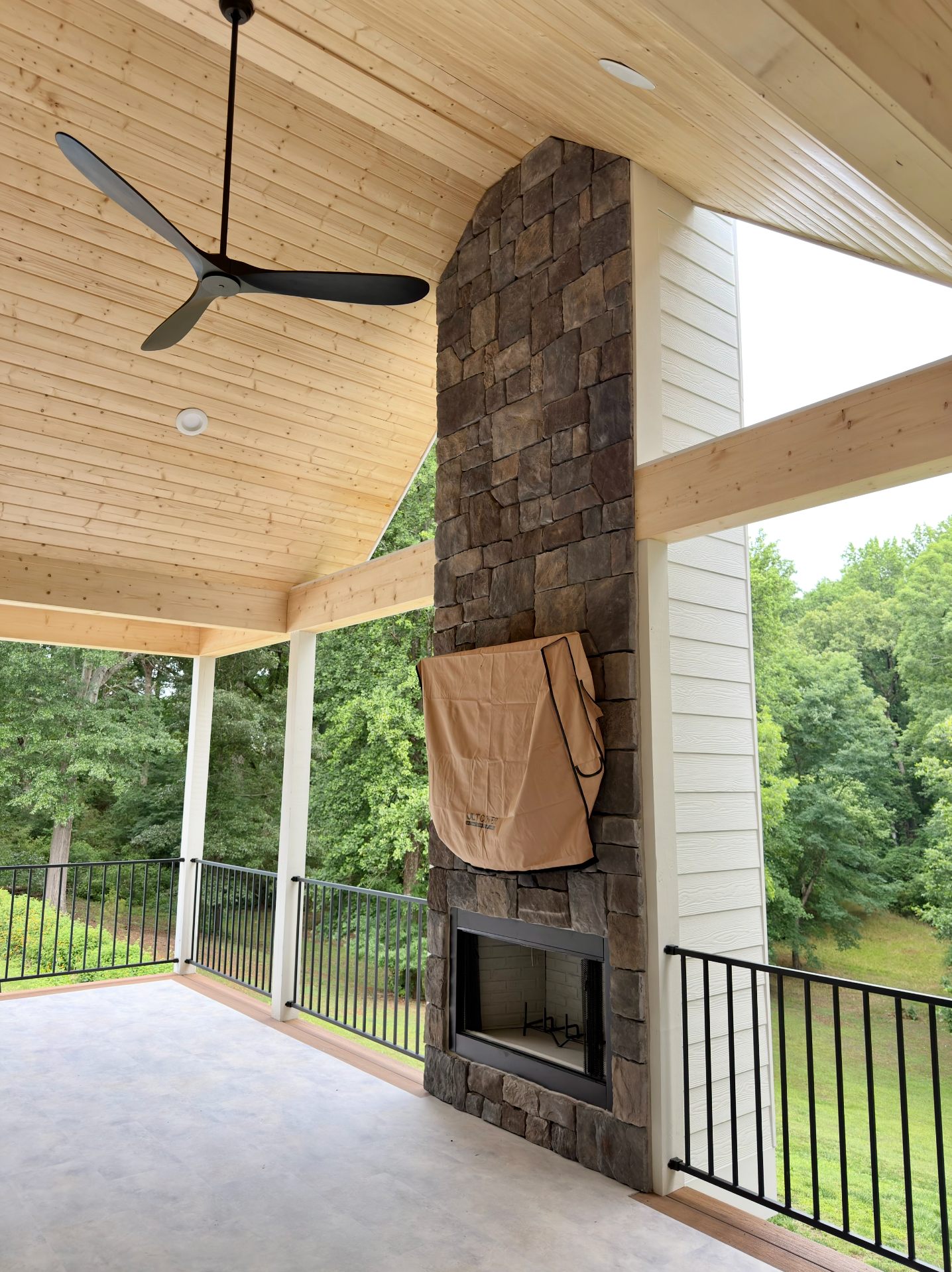 Covered porch with a floor-to-ceiling stacked-stone fireplace and tongue-and-groove wood ceiling