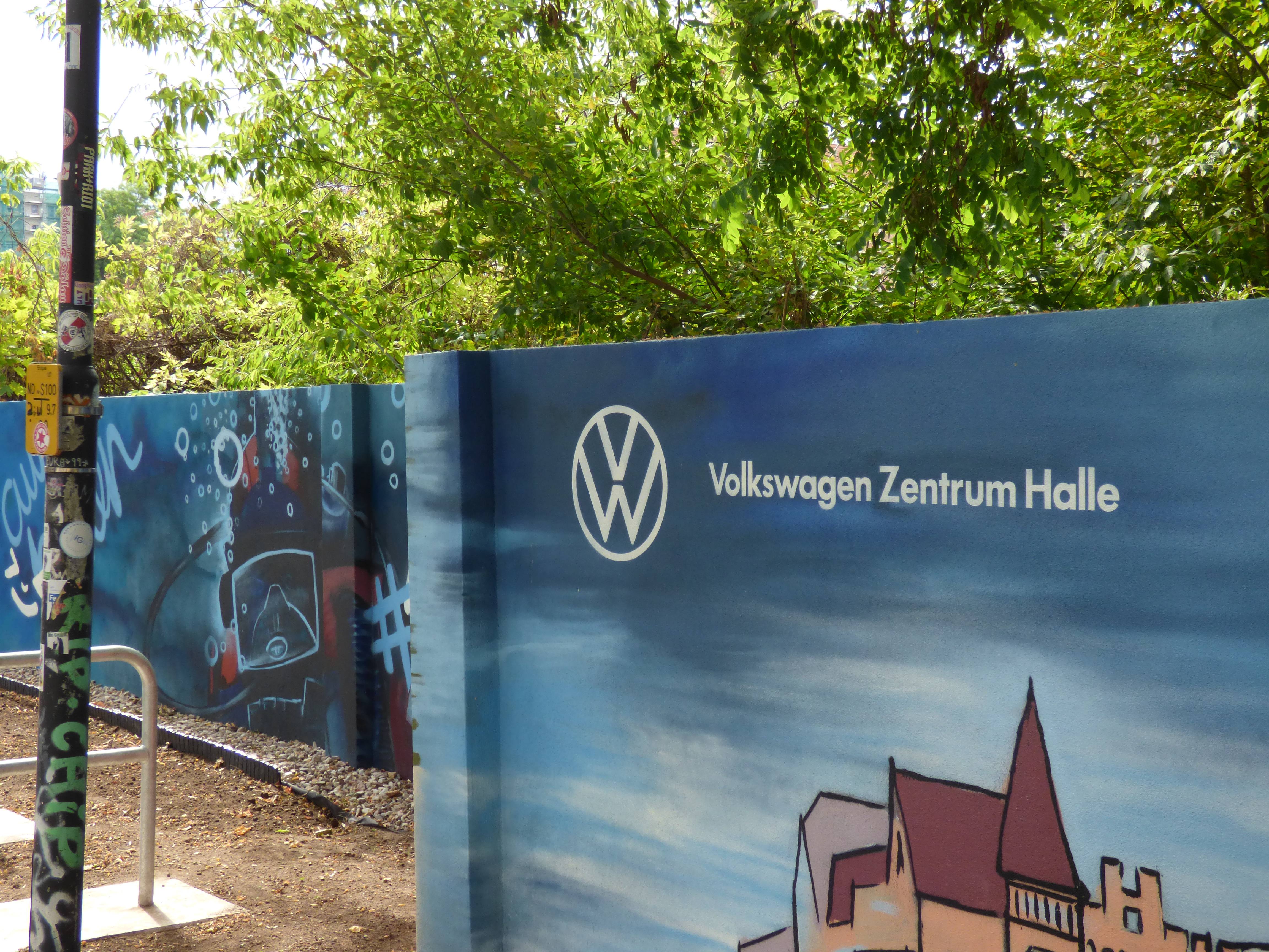 Blaues Wandbild am Volkswagen Zentrum Halle mit Stadtmotiv und grünen Bäumen im Hintergrund