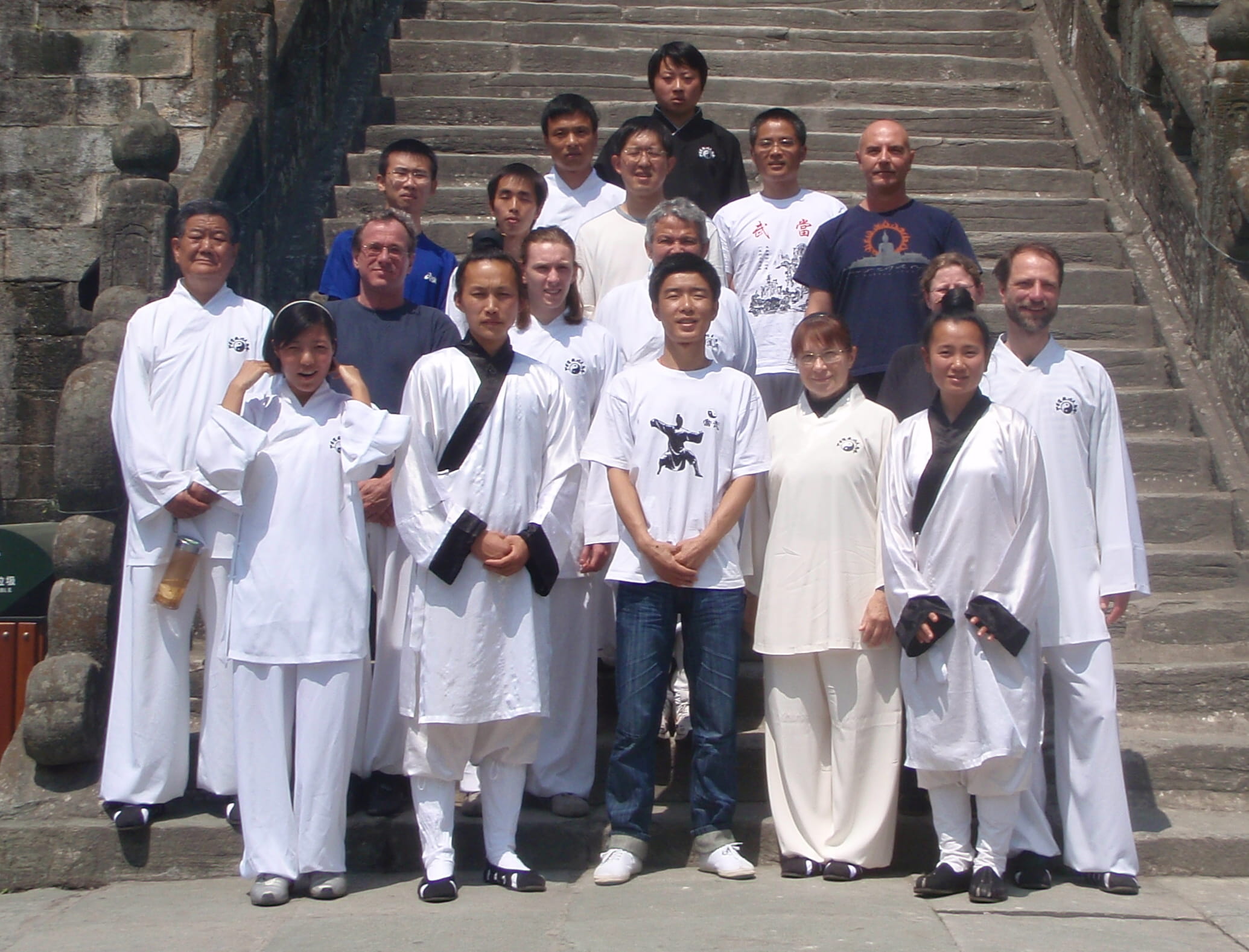 Group of students and Kadama in white qigong robes on temple steps, sunny day, formal certification group photo