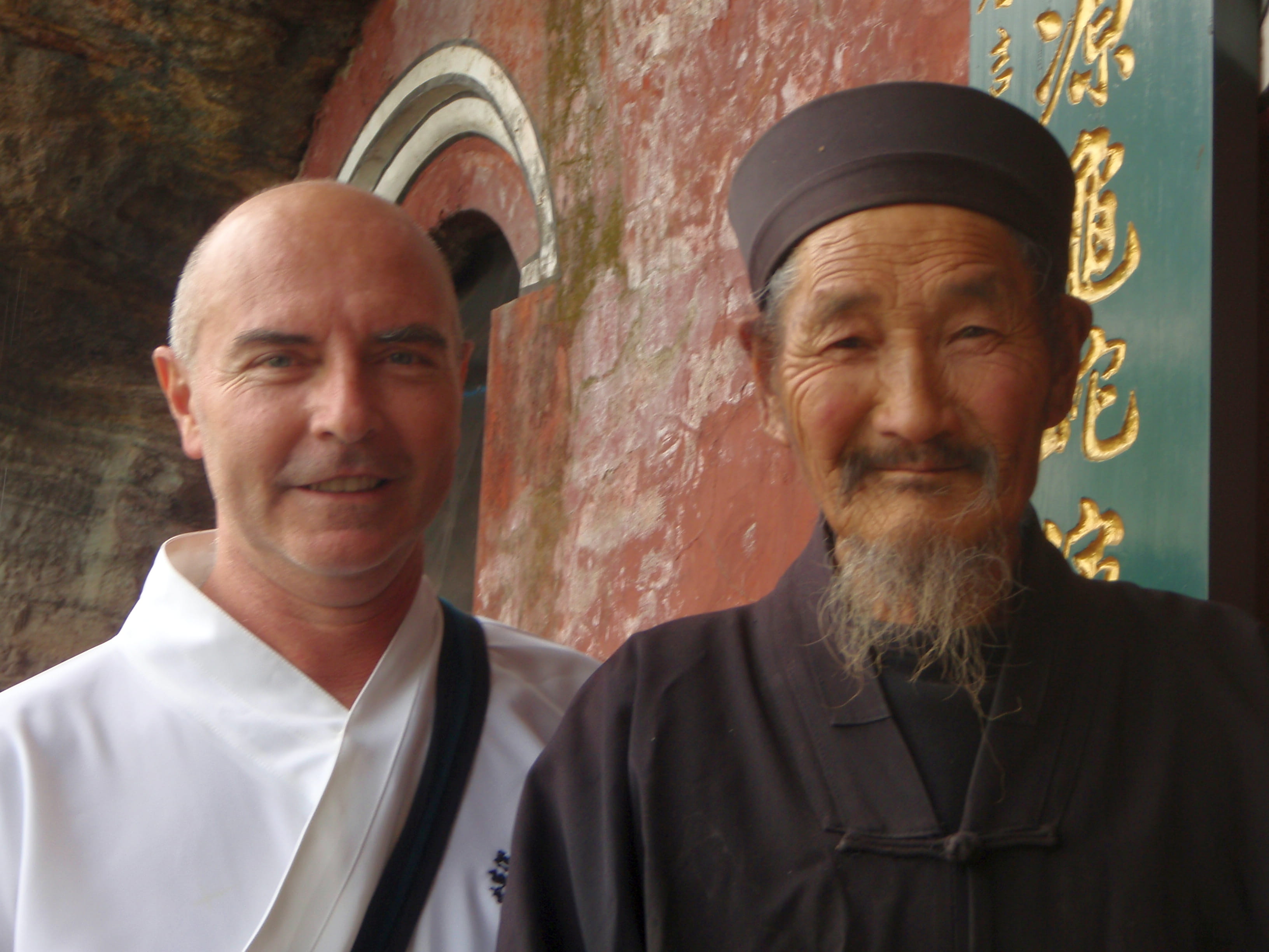 Kadama with his elderly Chinese master in traditional robes, standing together near a temple doorway