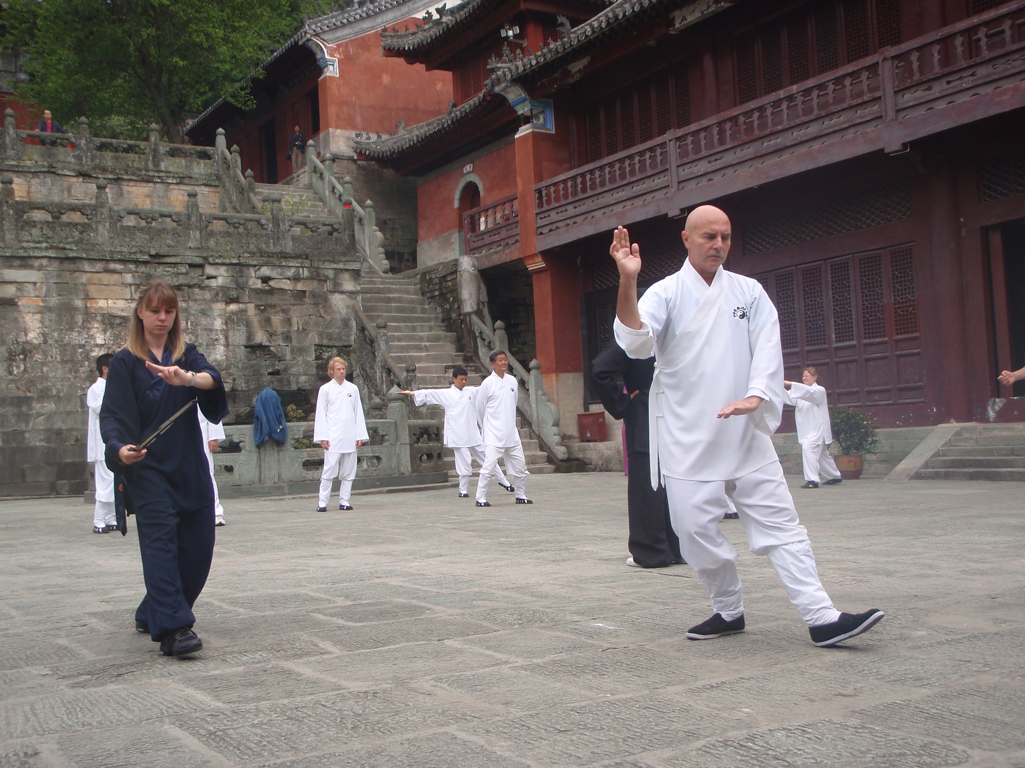 Female student with wooden sword and Kadama practising in a temple courtyard, other students visible in background