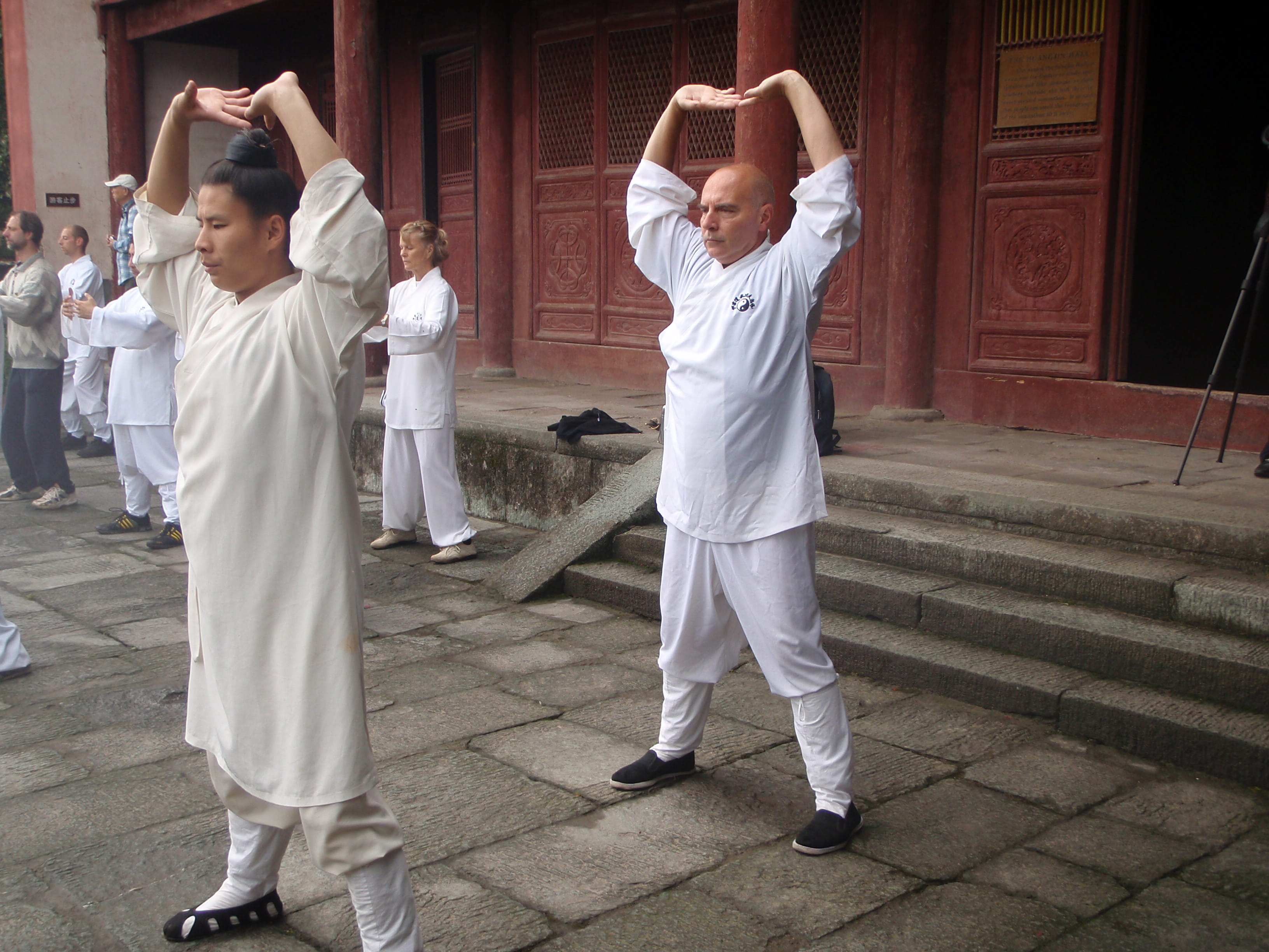 Kadama and female student practising coordinated arm movements in front of ornate red temple doors