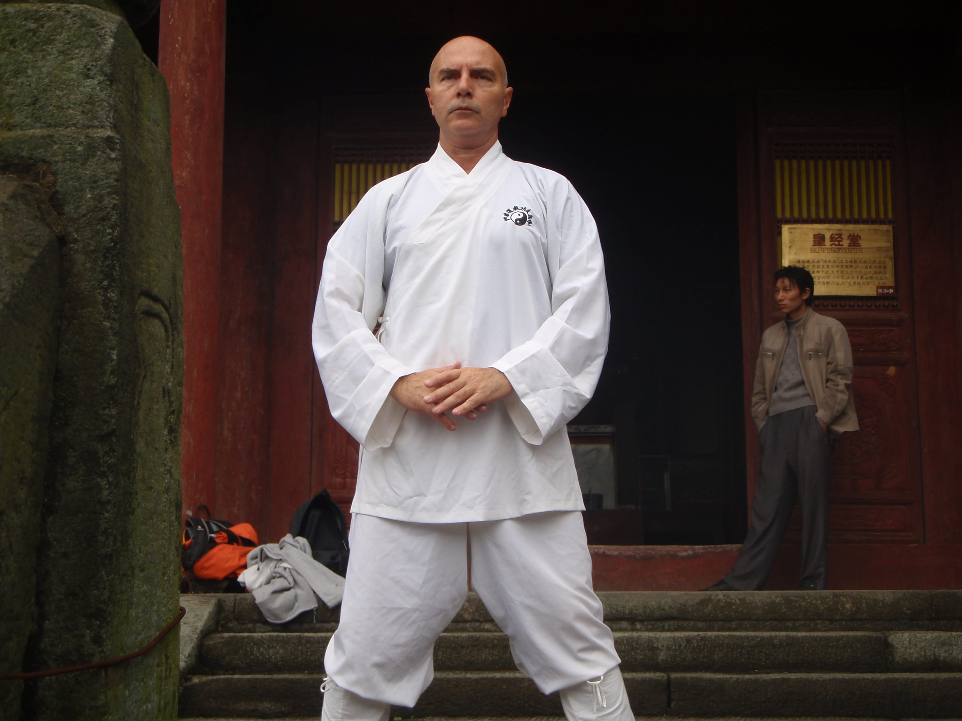 Kadama in a centered stance practising qigong on temple steps with dark wood and stone pillars behind him