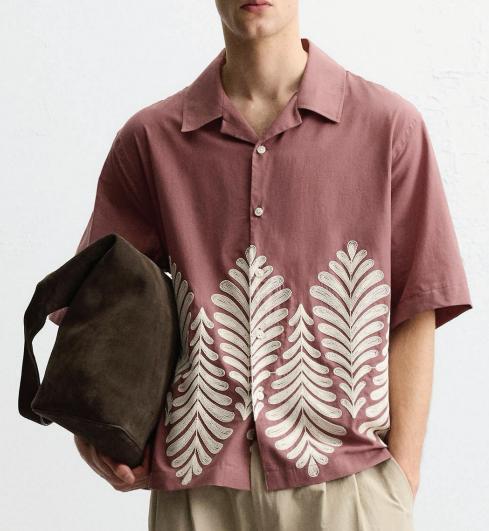 Model wearing a rose short-sleeve shirt with ivory botanical embroidery.