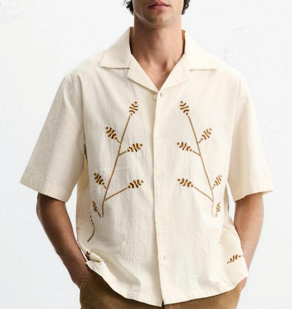 Model wearing an ivory short-sleeve shirt with delicate botanical embroidery.