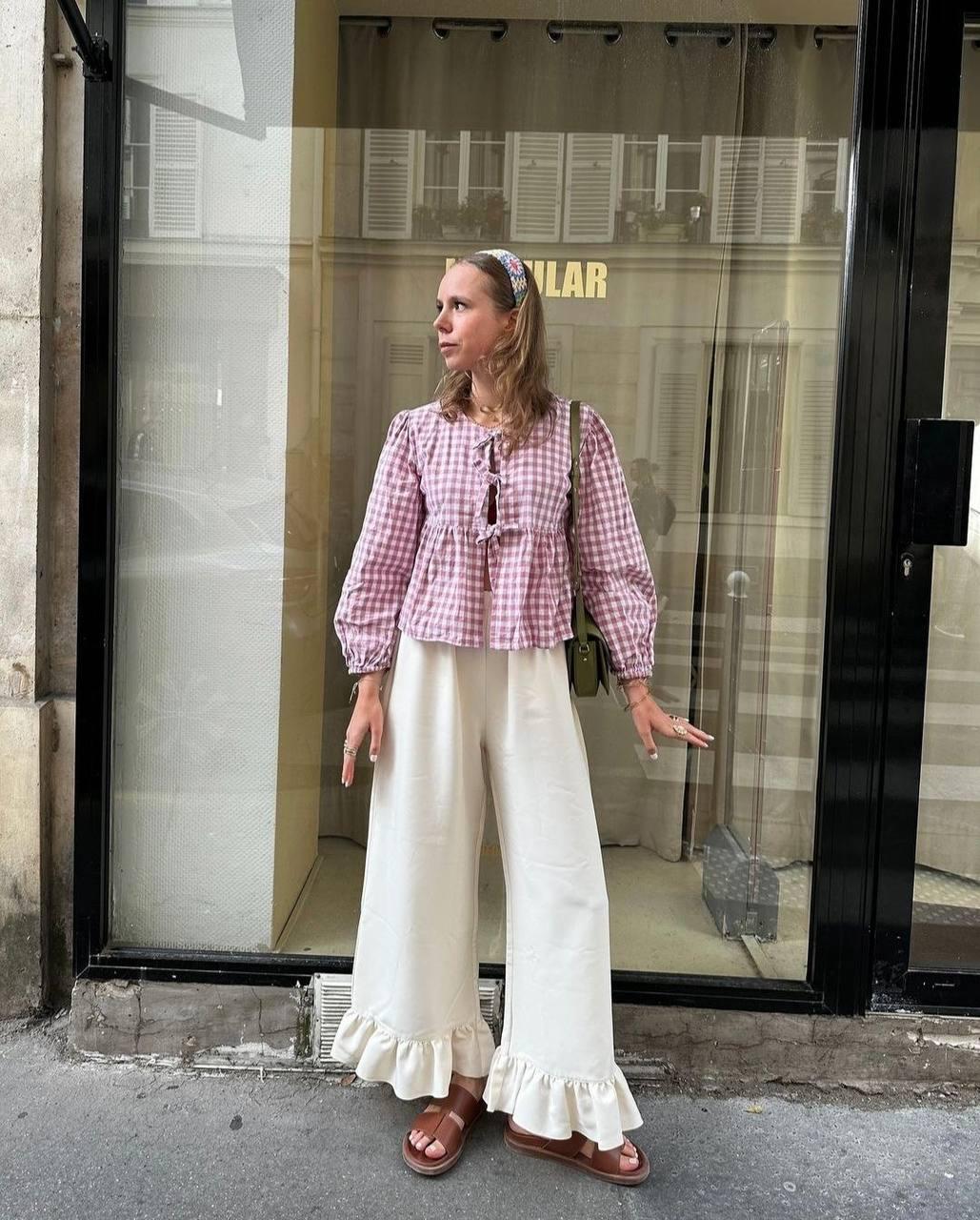 Model wearing a pink gingham tie-front blouse with ivory ruffle-hem trousers.