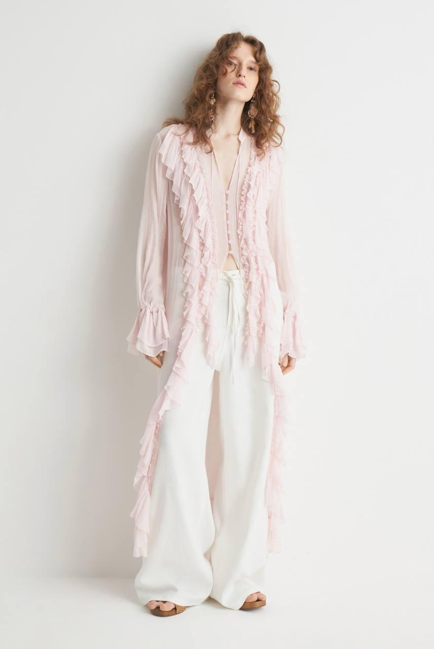 Model wearing a pale pink long blouse with cascading ruffles and flared cuffs.