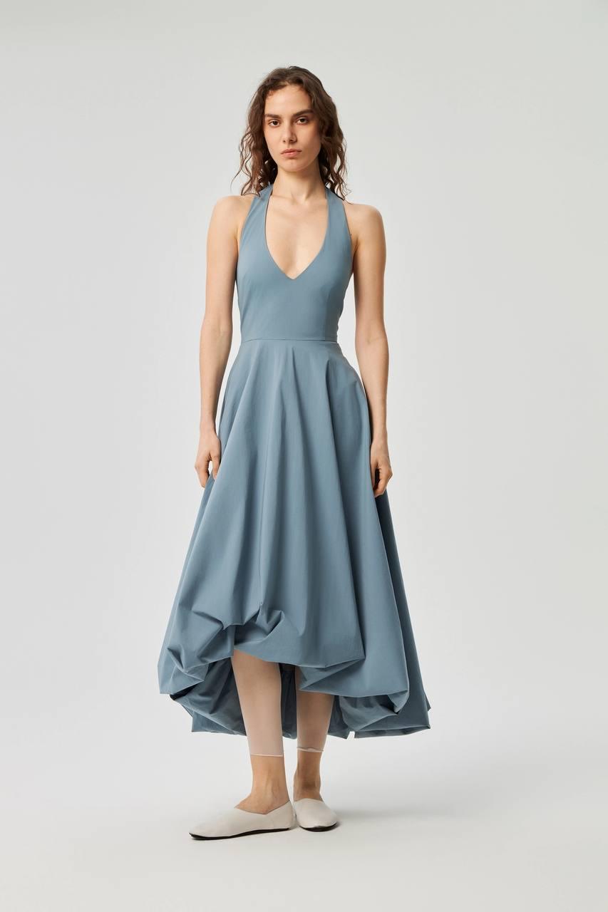 Model wearing a slate-blue halter dress with a full high-low skirt.