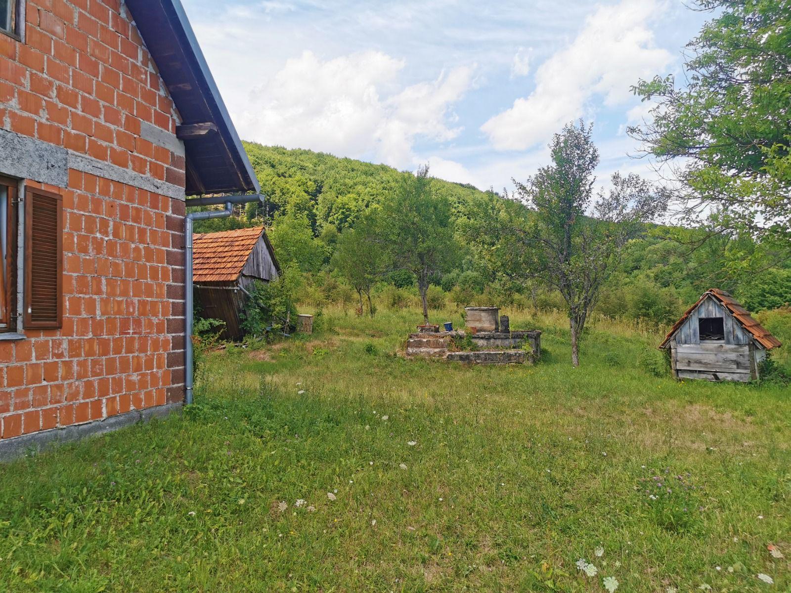 Bočni zid opečne kuće s dvorištem i drvenim šupicama u okolici