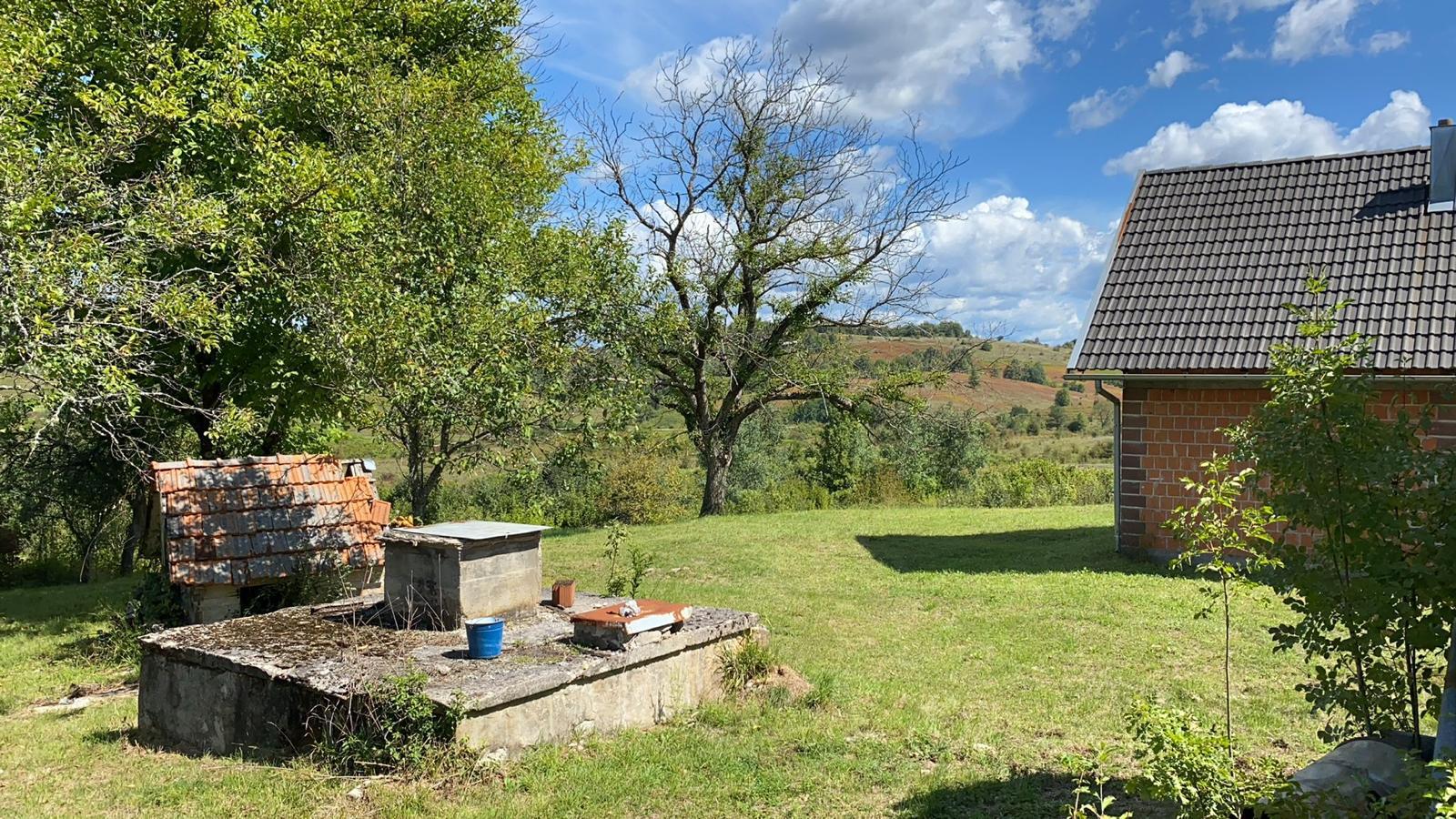 Bočni pogled na kuću s dvorištem, bunarom i starim drvetima