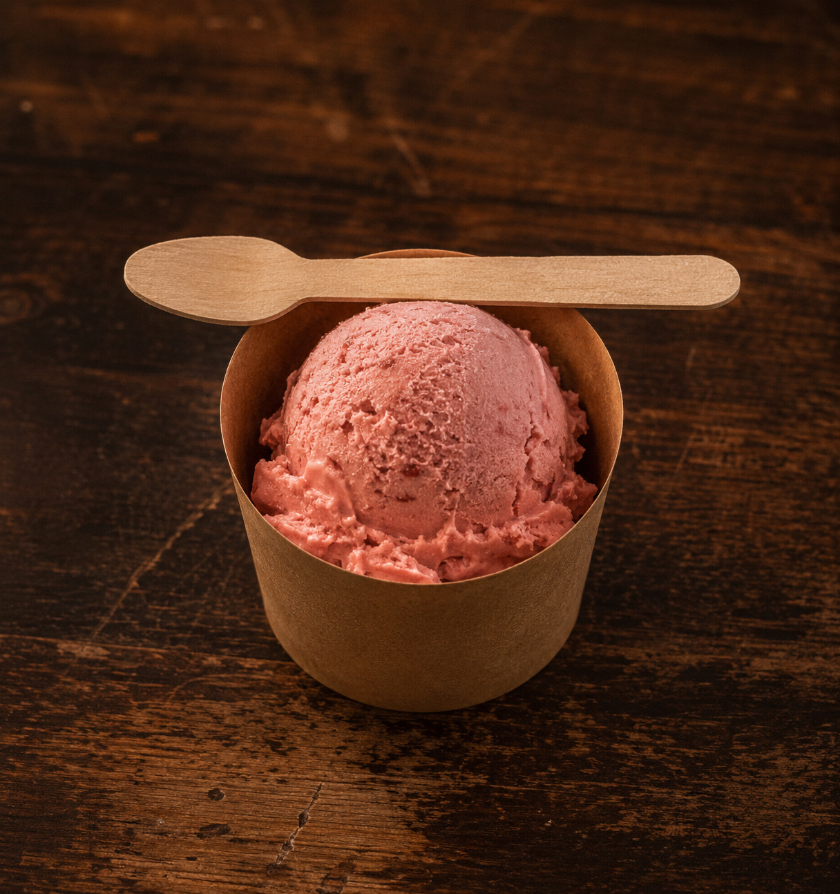 Kraft paper cup with a bright scoop and wooden spoon on worn wood surface
