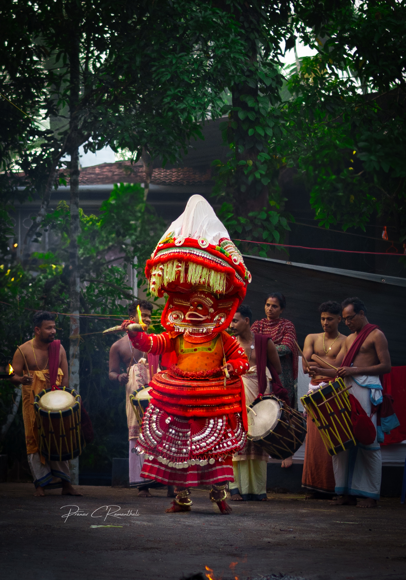 Theyyam performer in traditional red costume with musicians