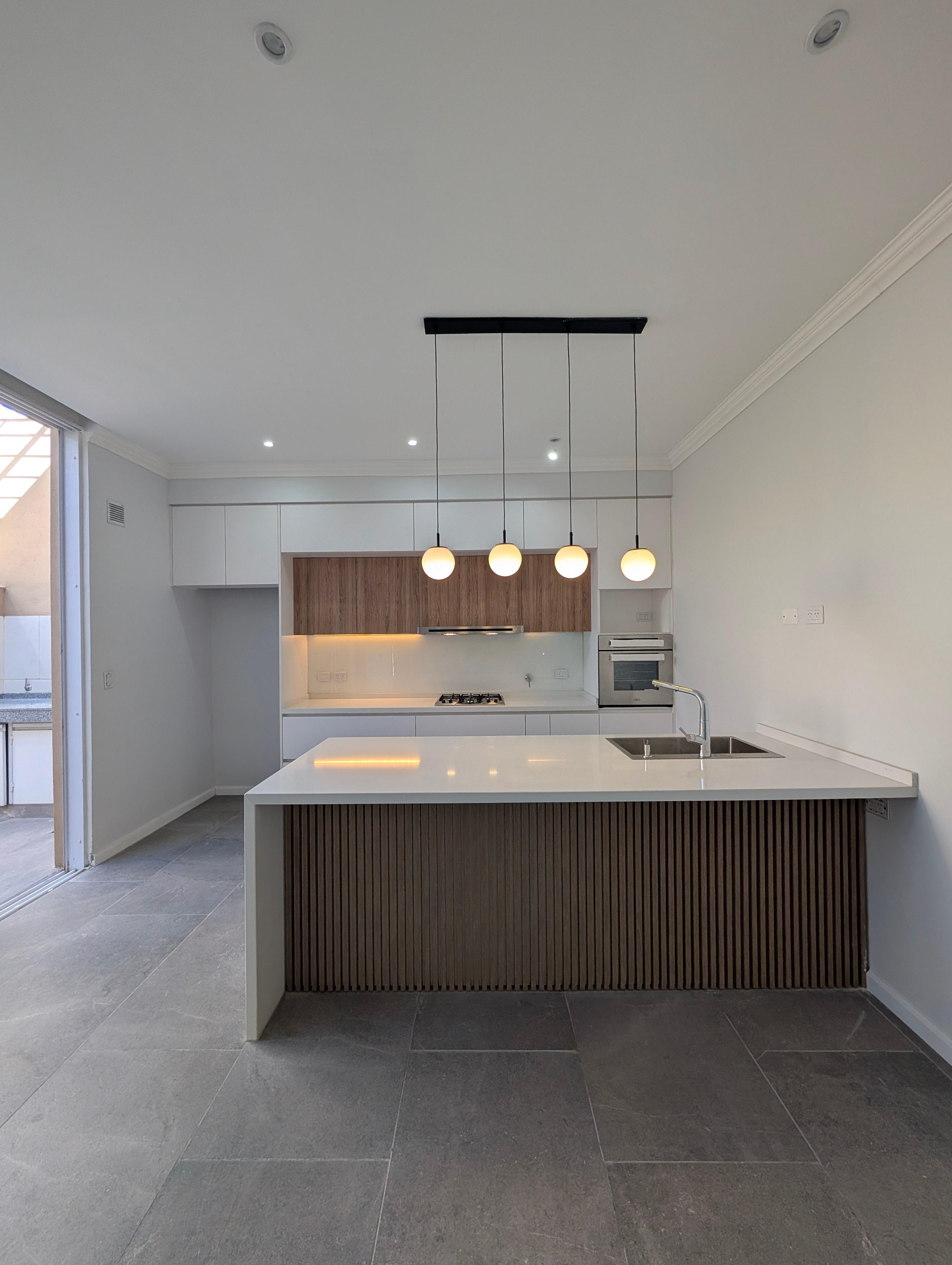 Cocina con iluminación cálida, lámparas encendidas y backsplash de madera