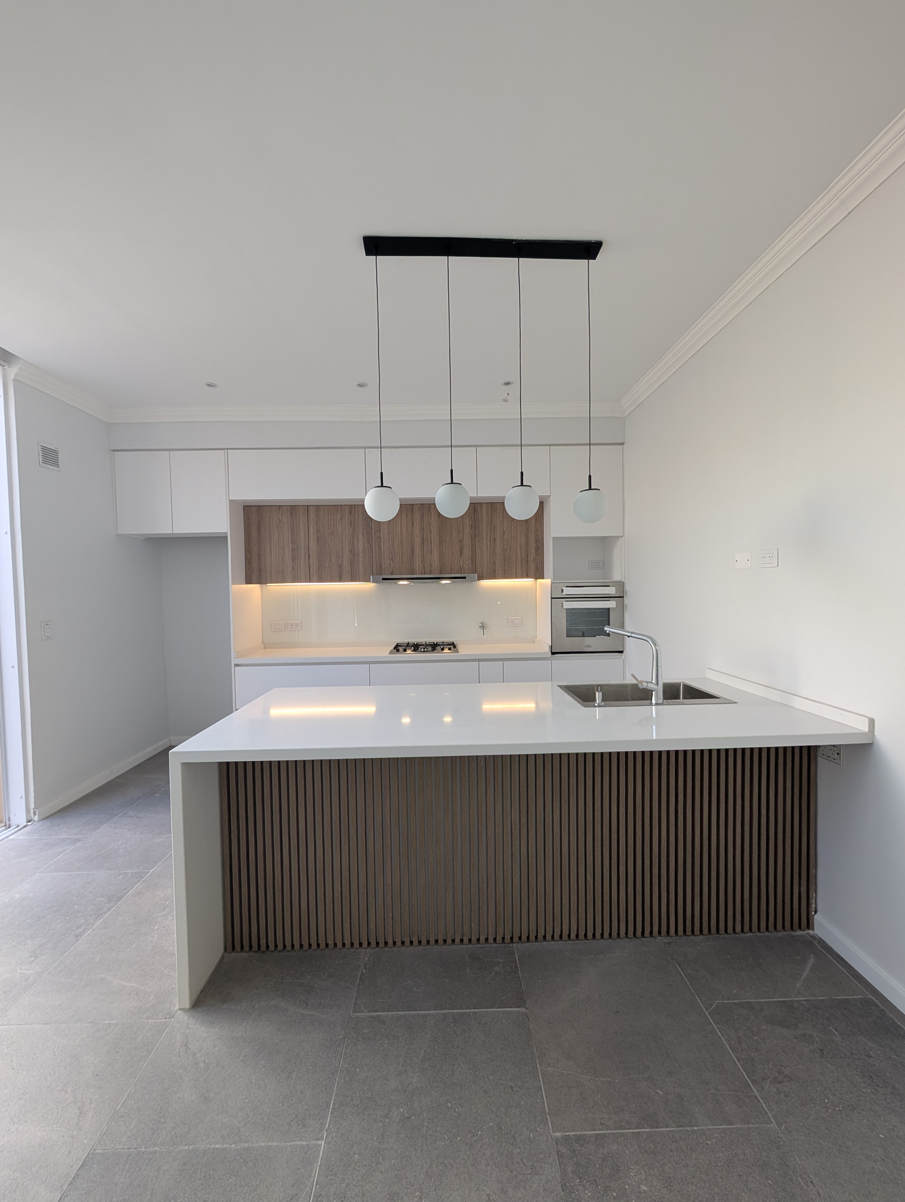 Cocina frontal con isla de listones de madera, mesada blanca y lámparas colgantes esféricas
