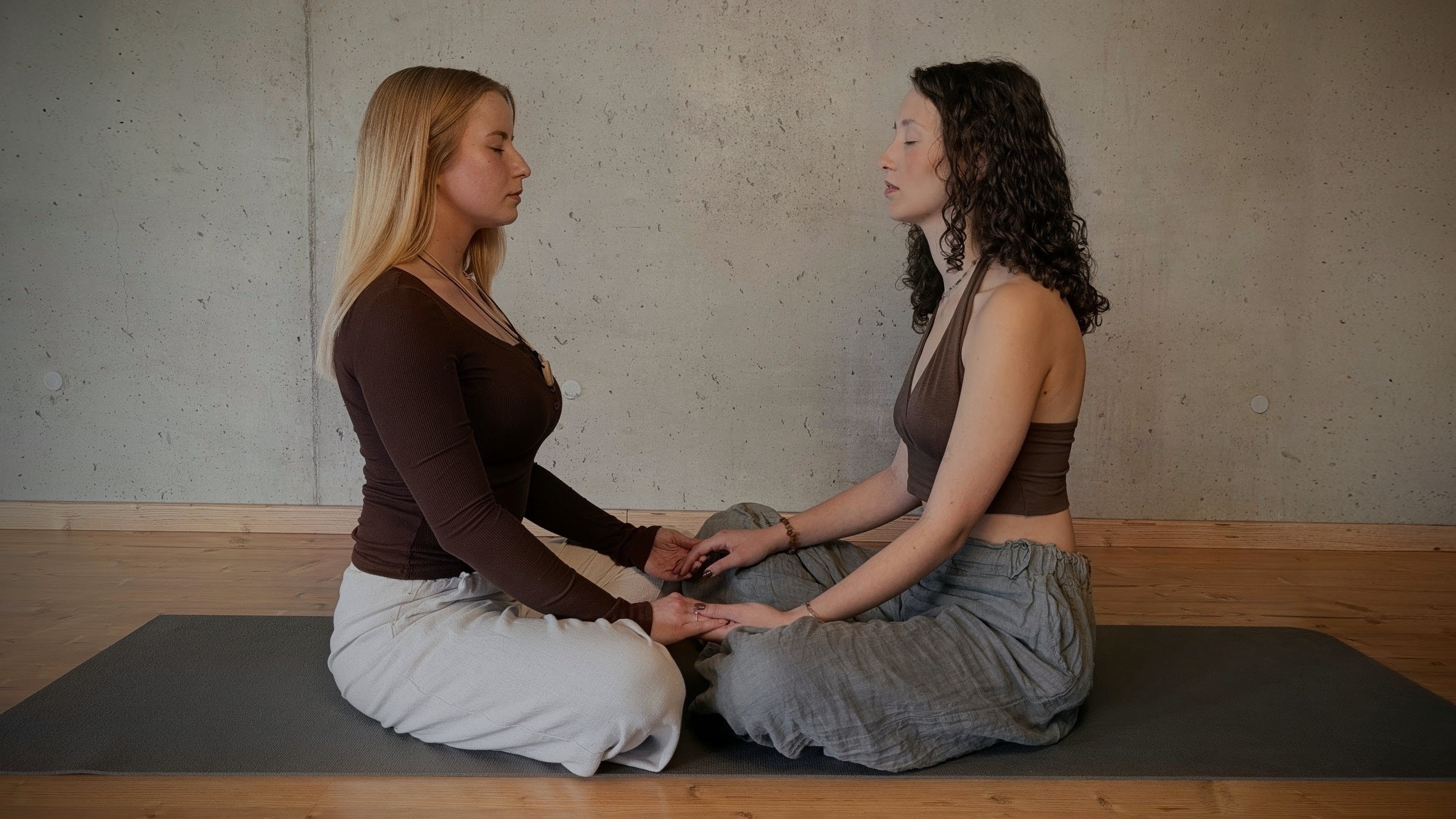 Two women sitting facing each other holding hands