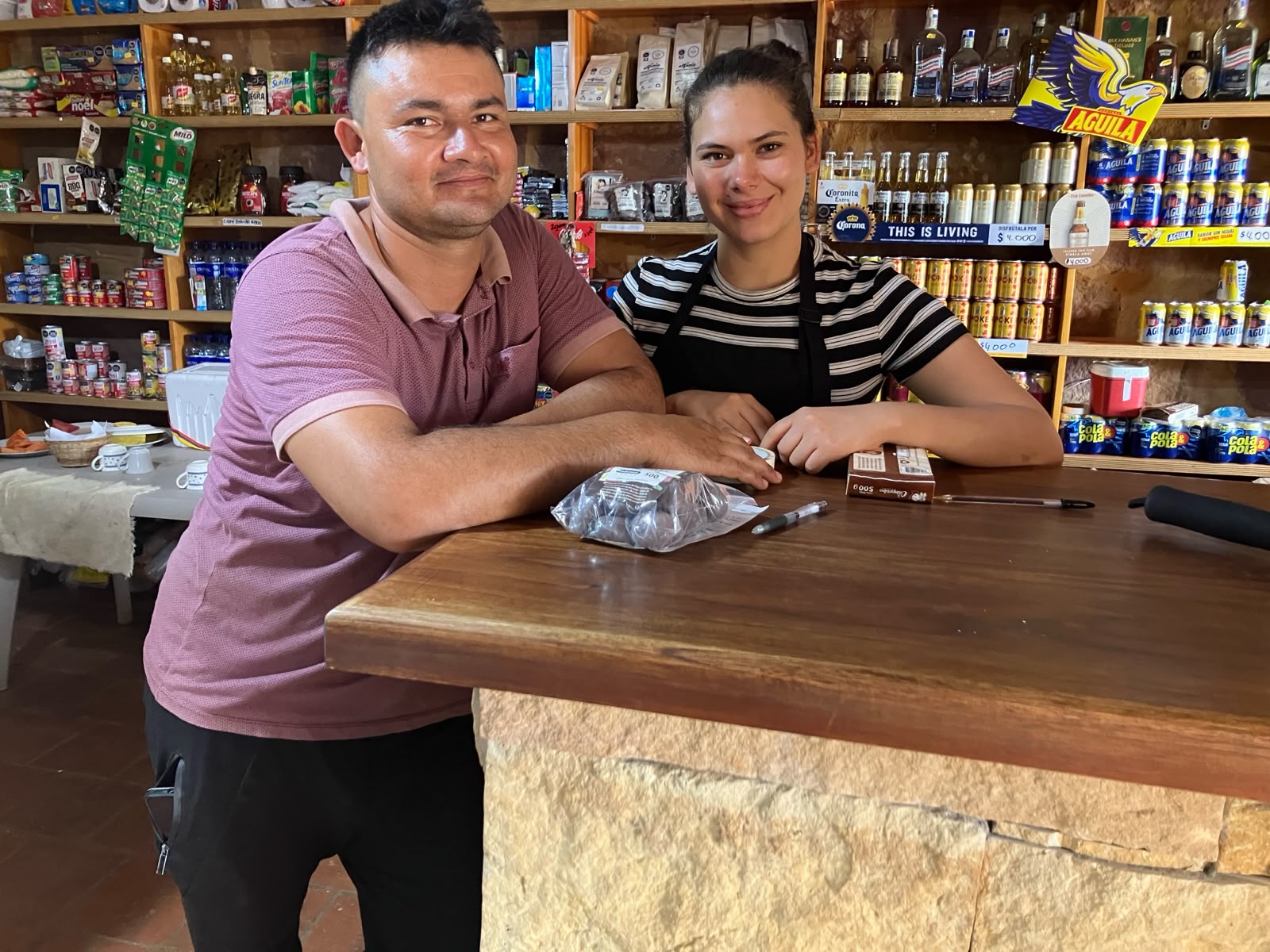 Heidi Meneses y Jorge Leonardo Jiménez apoyados en el mostrador de piedra de la tienda, con estantes de productos al fondo