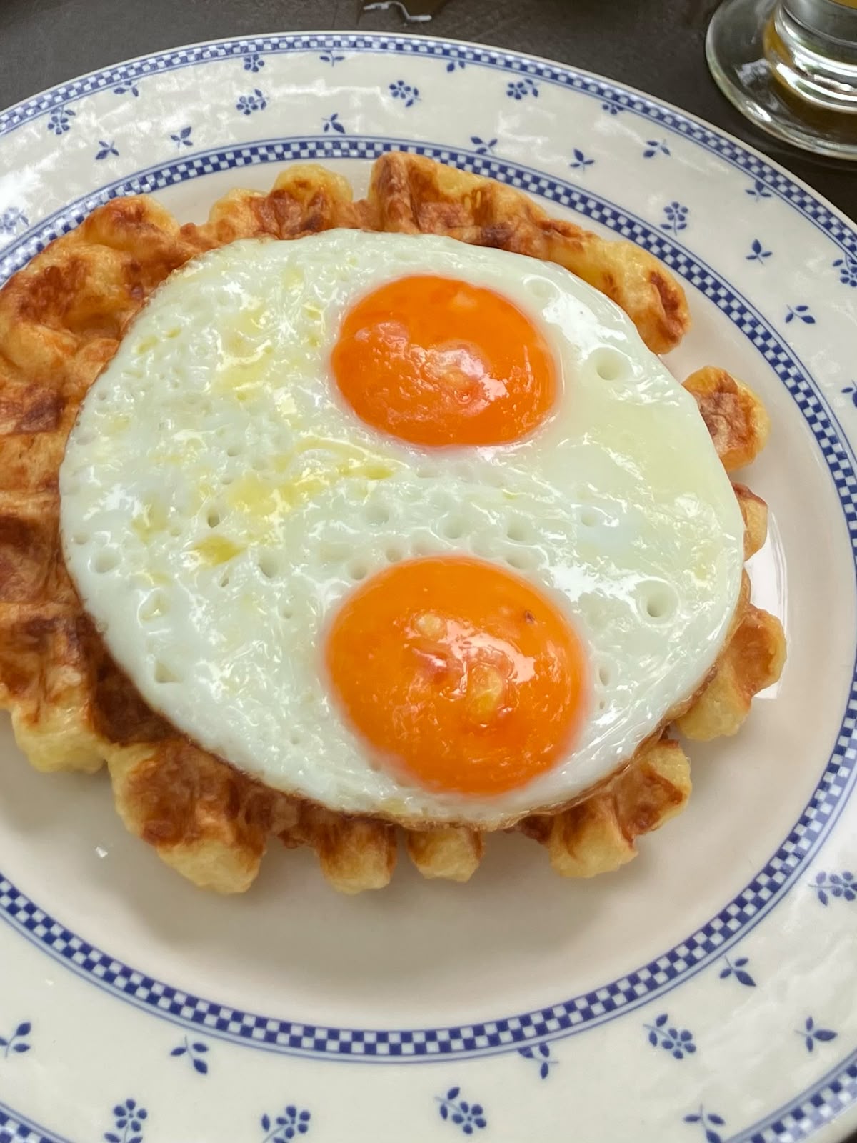 Waffle con dos huevos fritos de yema naranja sobre plato de cerámica azul y blanco