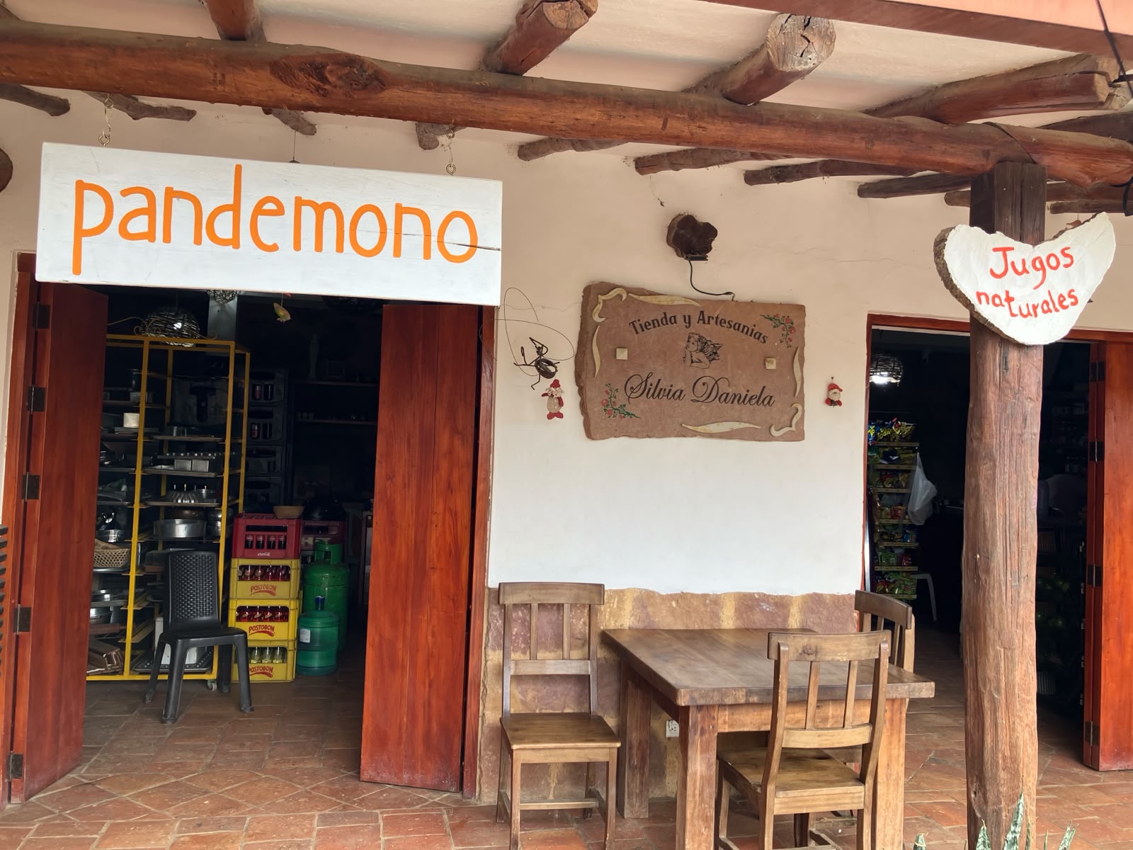 Fachada de Pandemono y Tienda y Artesanías Silvia Daniela con mesas de madera en el corredor