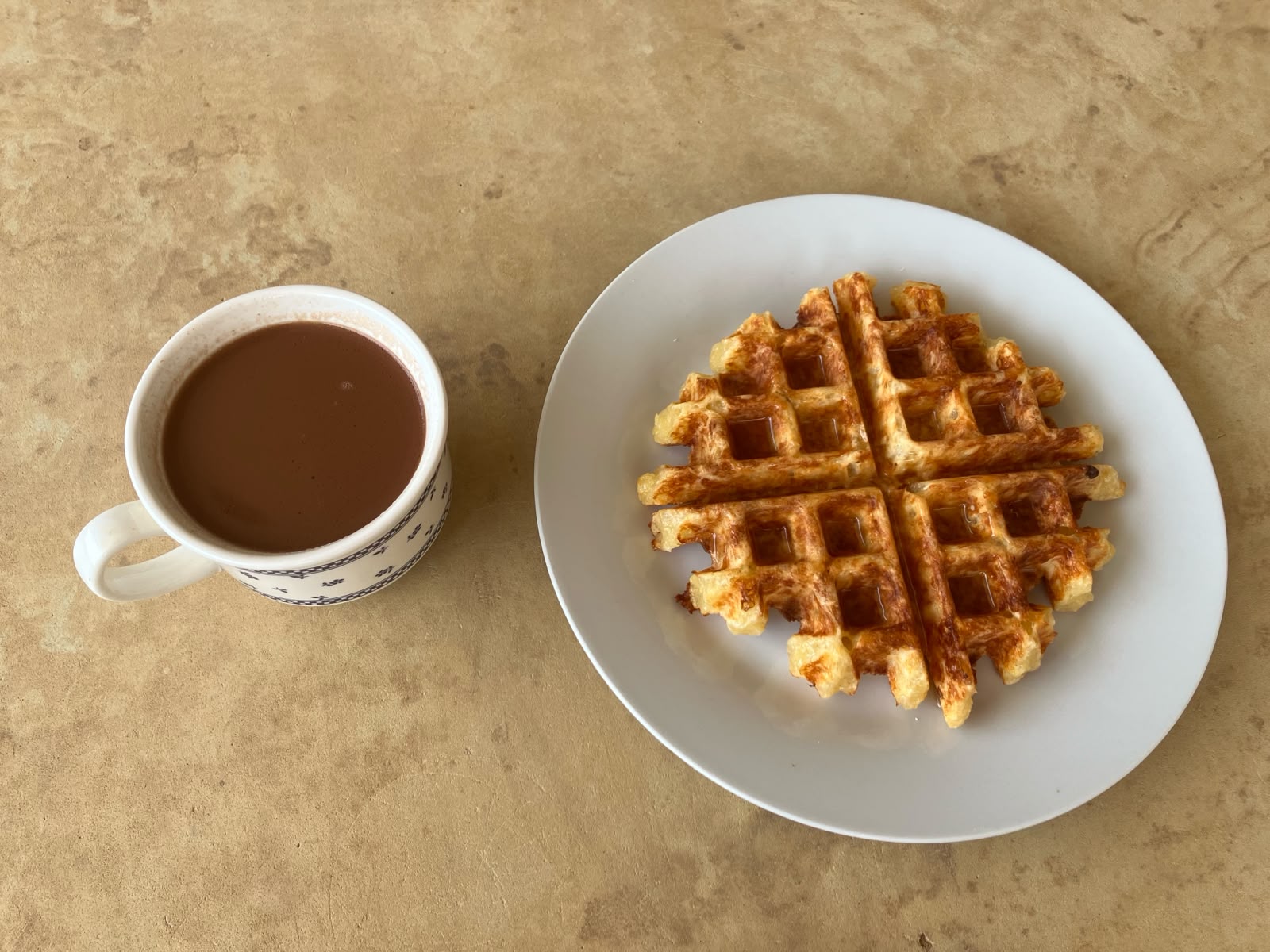 Waffle redondo en plato blanco junto a una taza de tinto