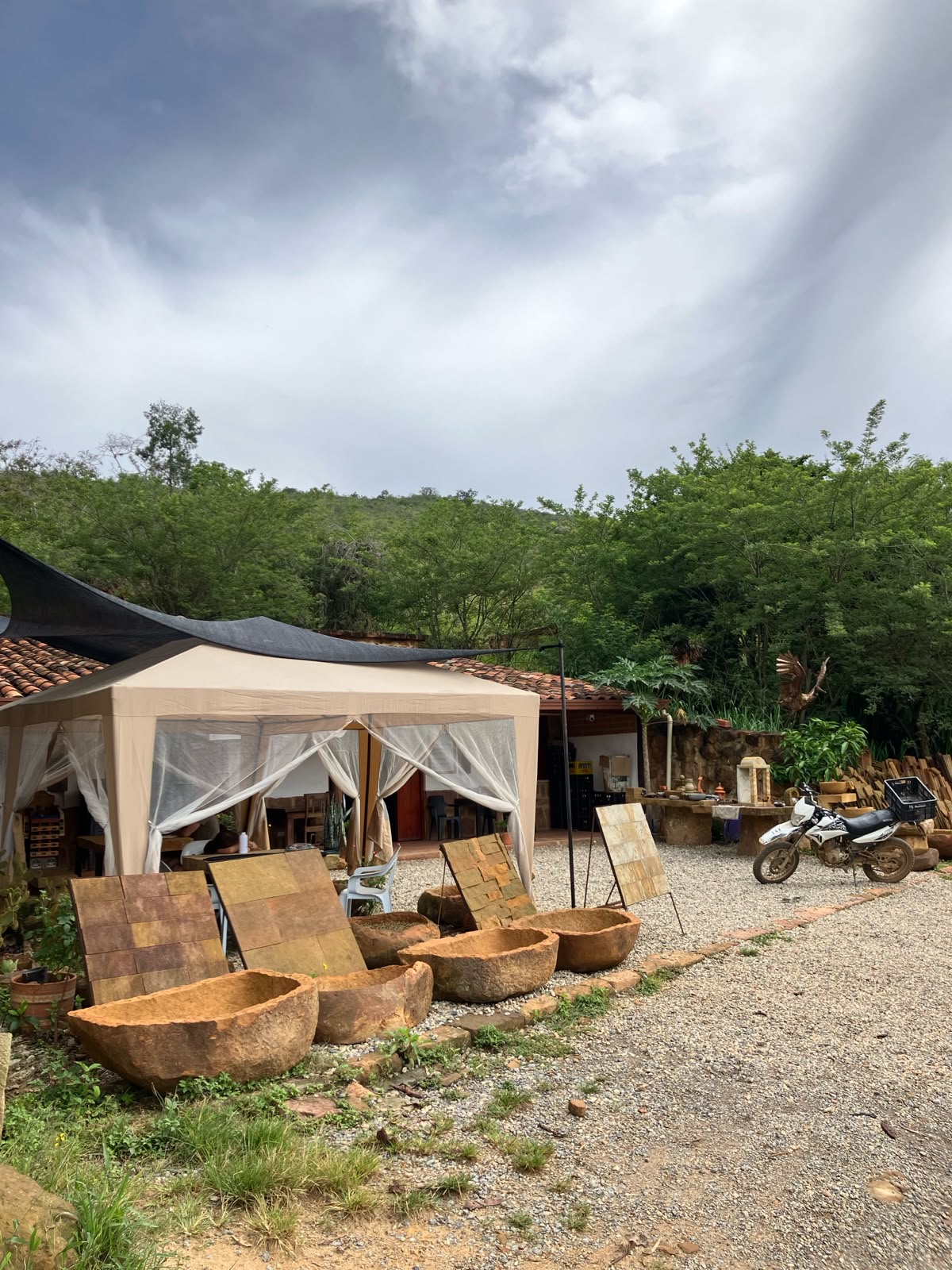 Vista exterior de la tienda con carpa beige, vasijas de piedra en el patio y naturaleza al fondo