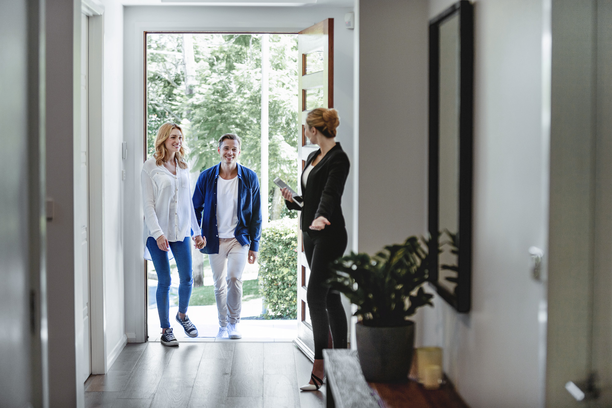 Real estate agent welcoming young couple at modern home entrance