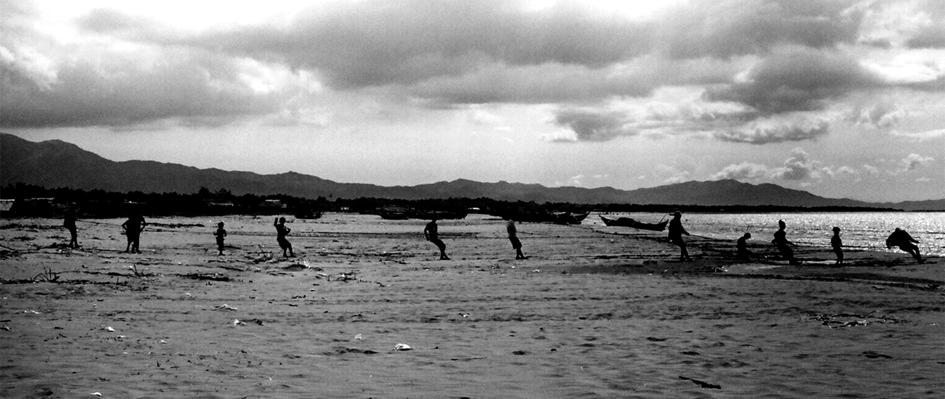 Beach scene with many people wading in shallow water against mountain backdrop