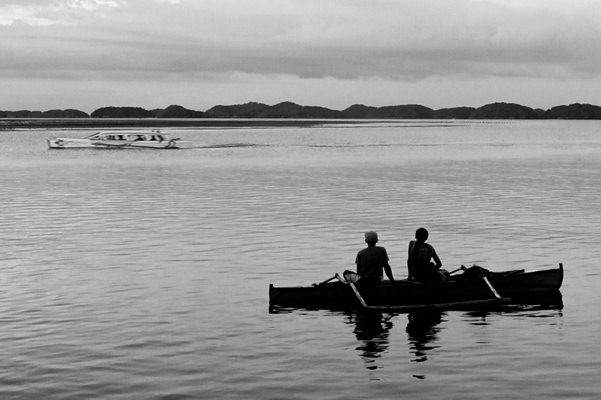Two men in small boat on water with island mountains visible in distant background