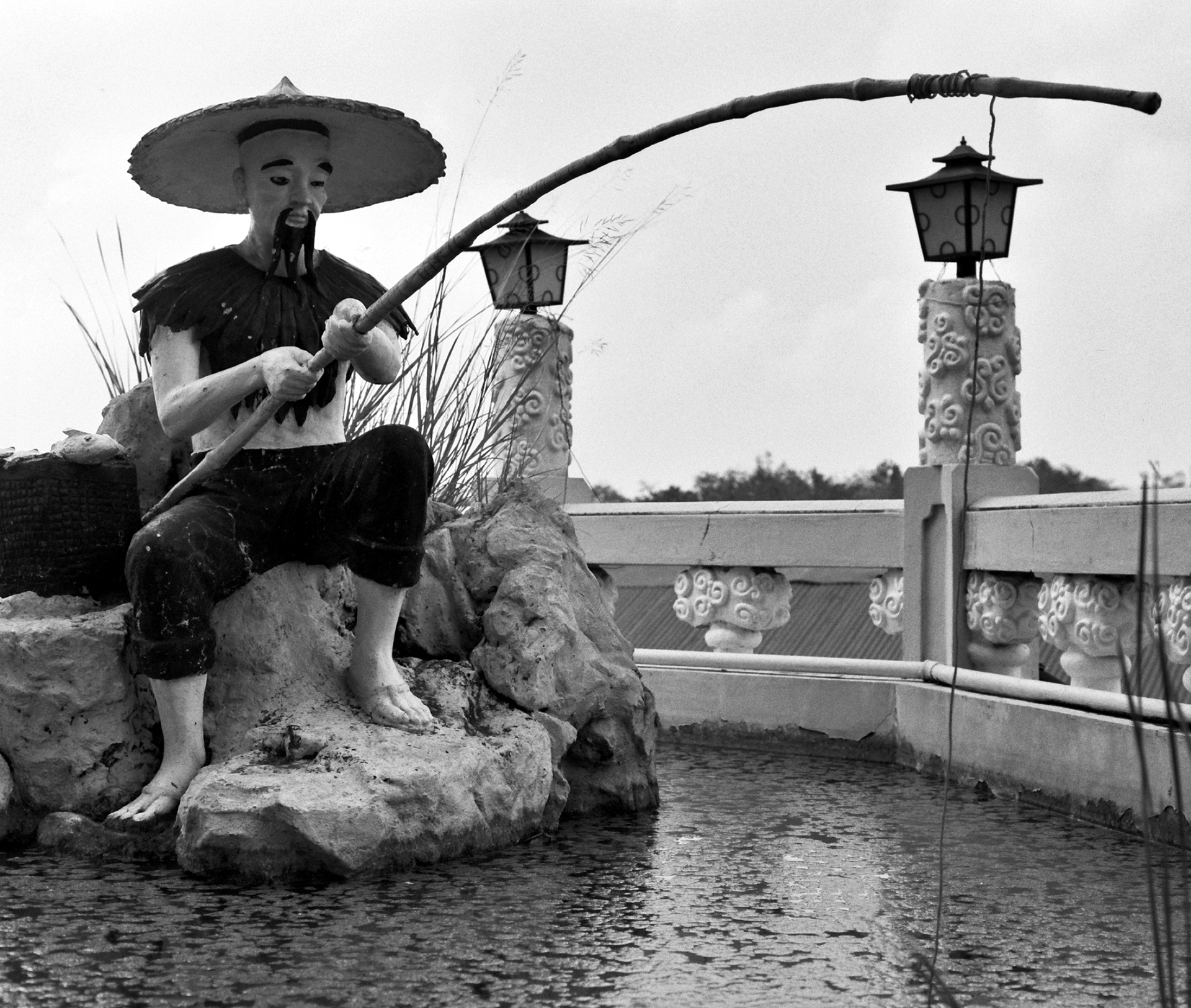 Man in wide-brimmed traditional hat fishing with net by ornamental water feature