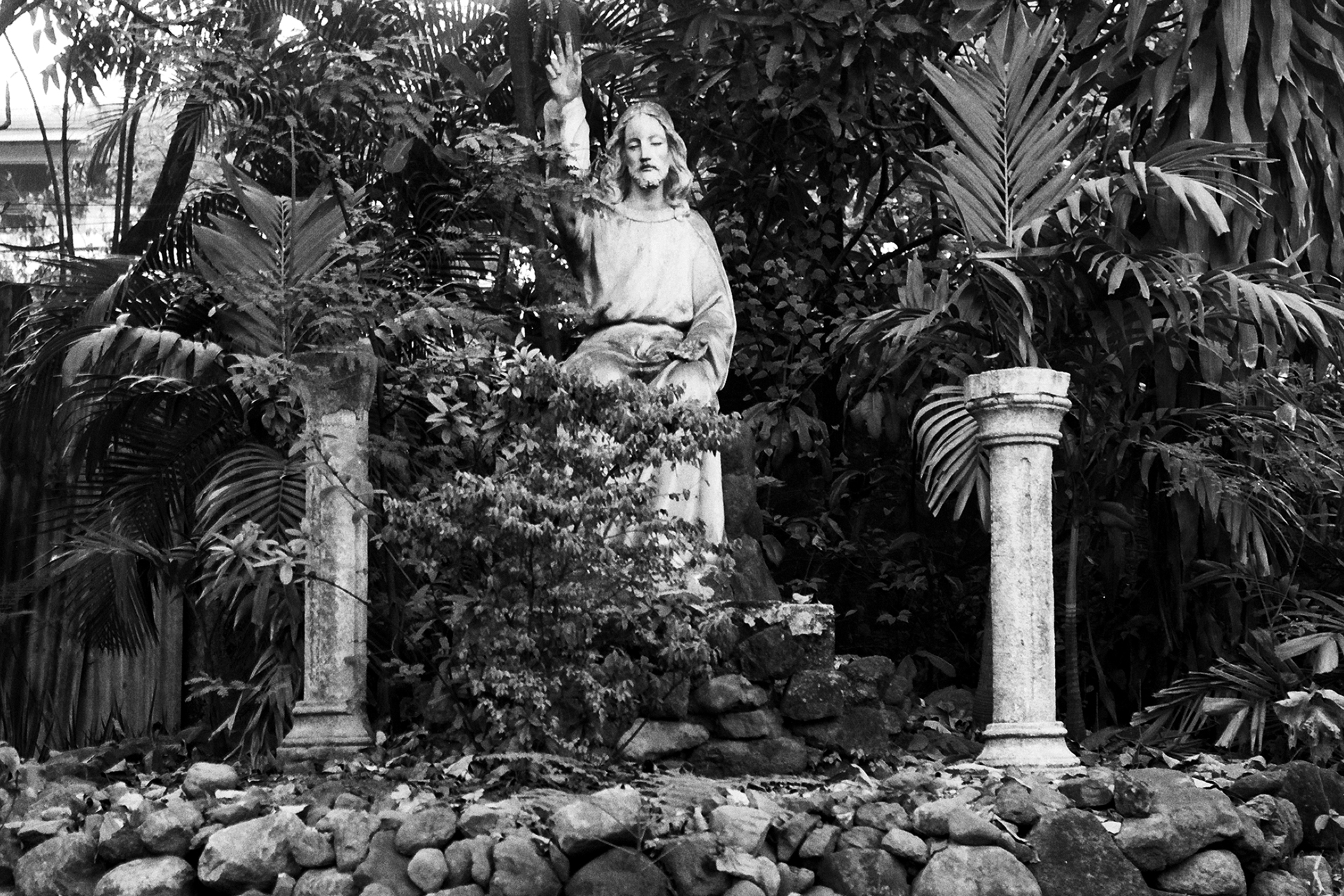 Religious garden statue surrounded by tropical vegetation and stone columns