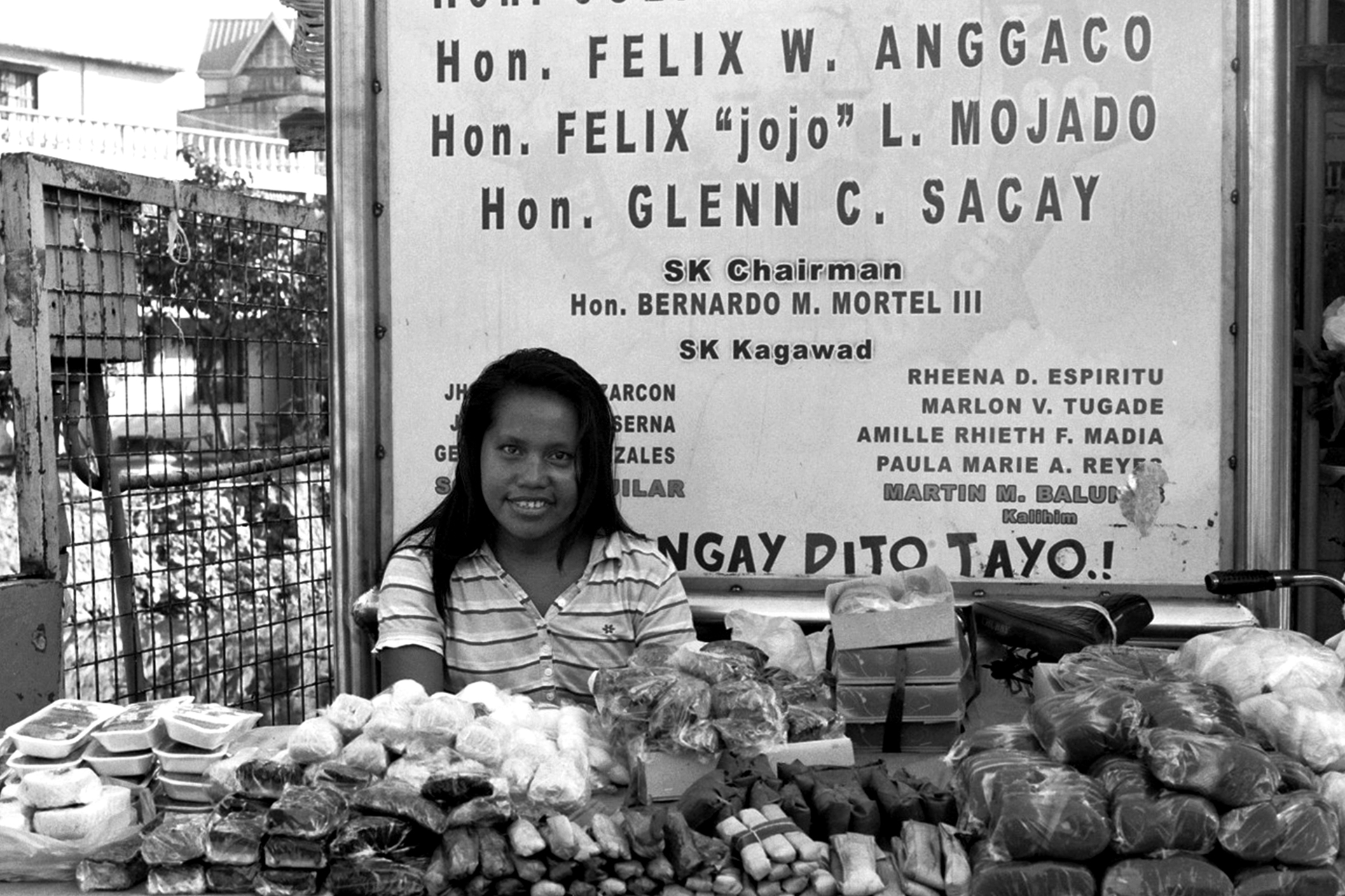 Woman vendor smiling at food market stall with packaged goods and merchandise displayed