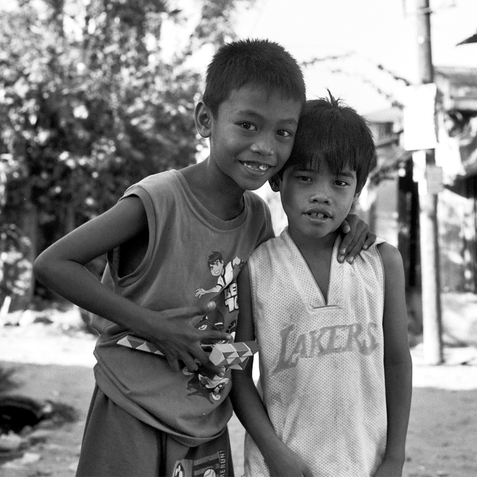 Two young boys with arms around each other smiling outdoors