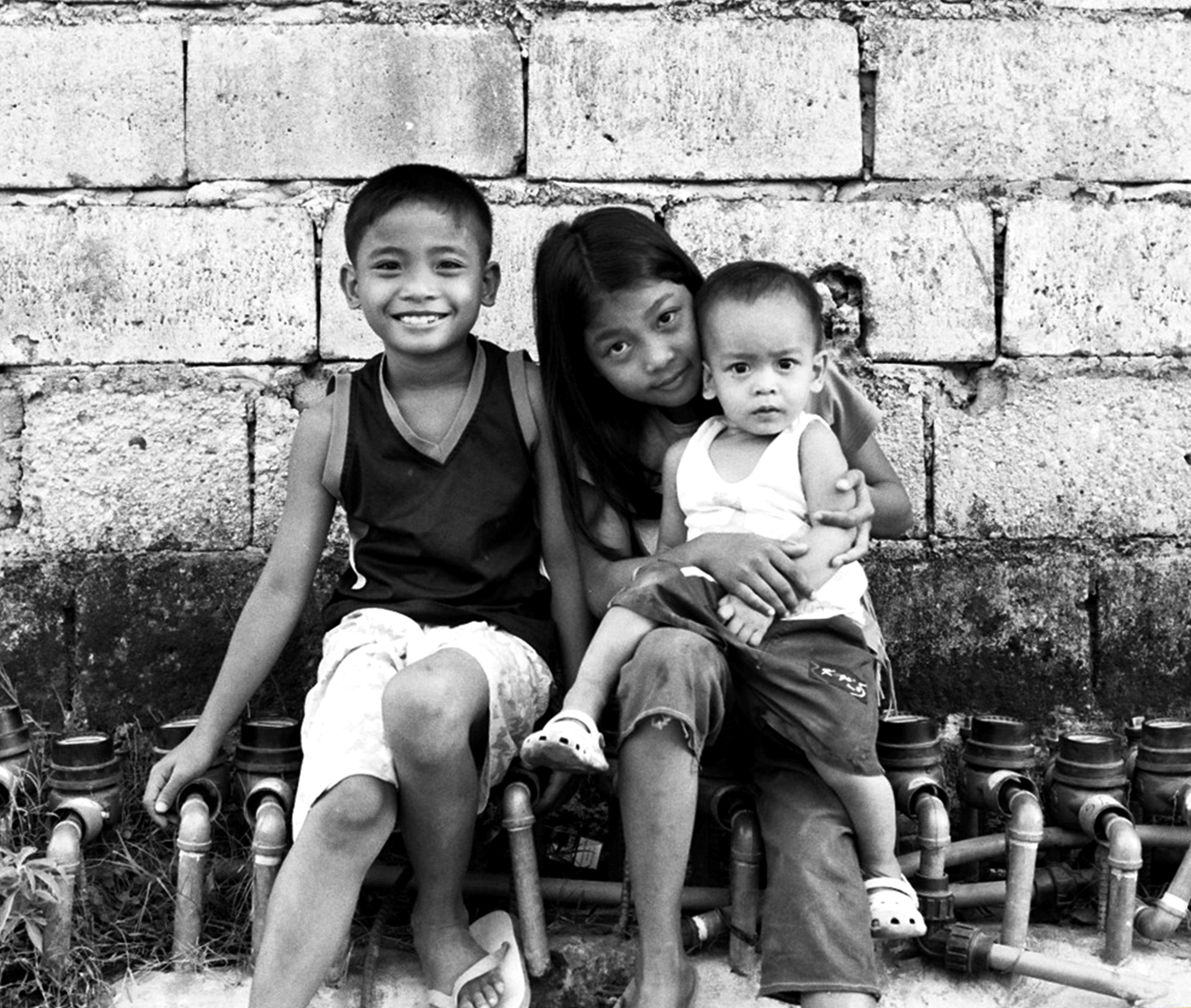 Young woman holding two small children against large stone block wall
