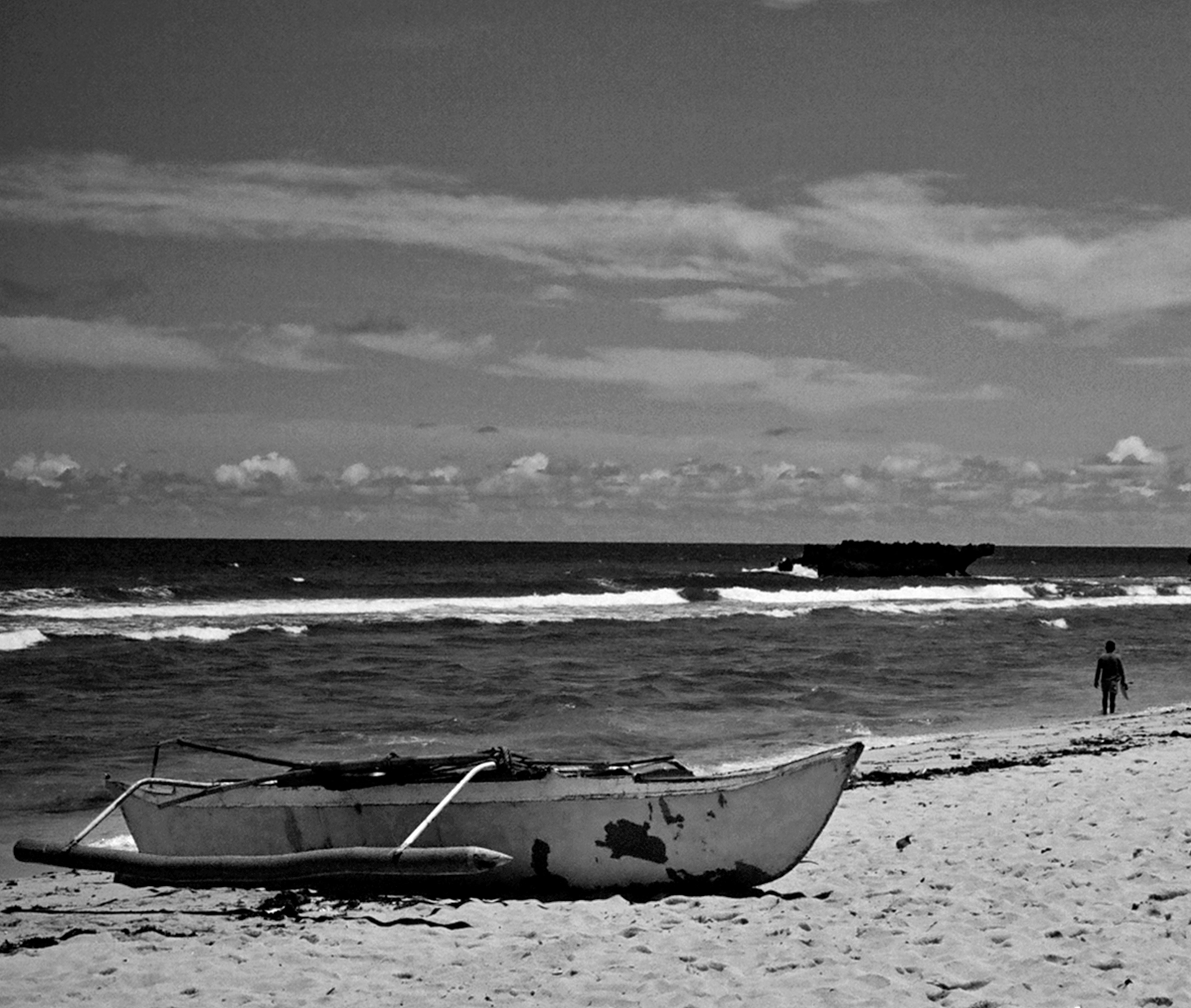 Beach scene with two fishing boats on sand person wading in ocean with dramatic sky