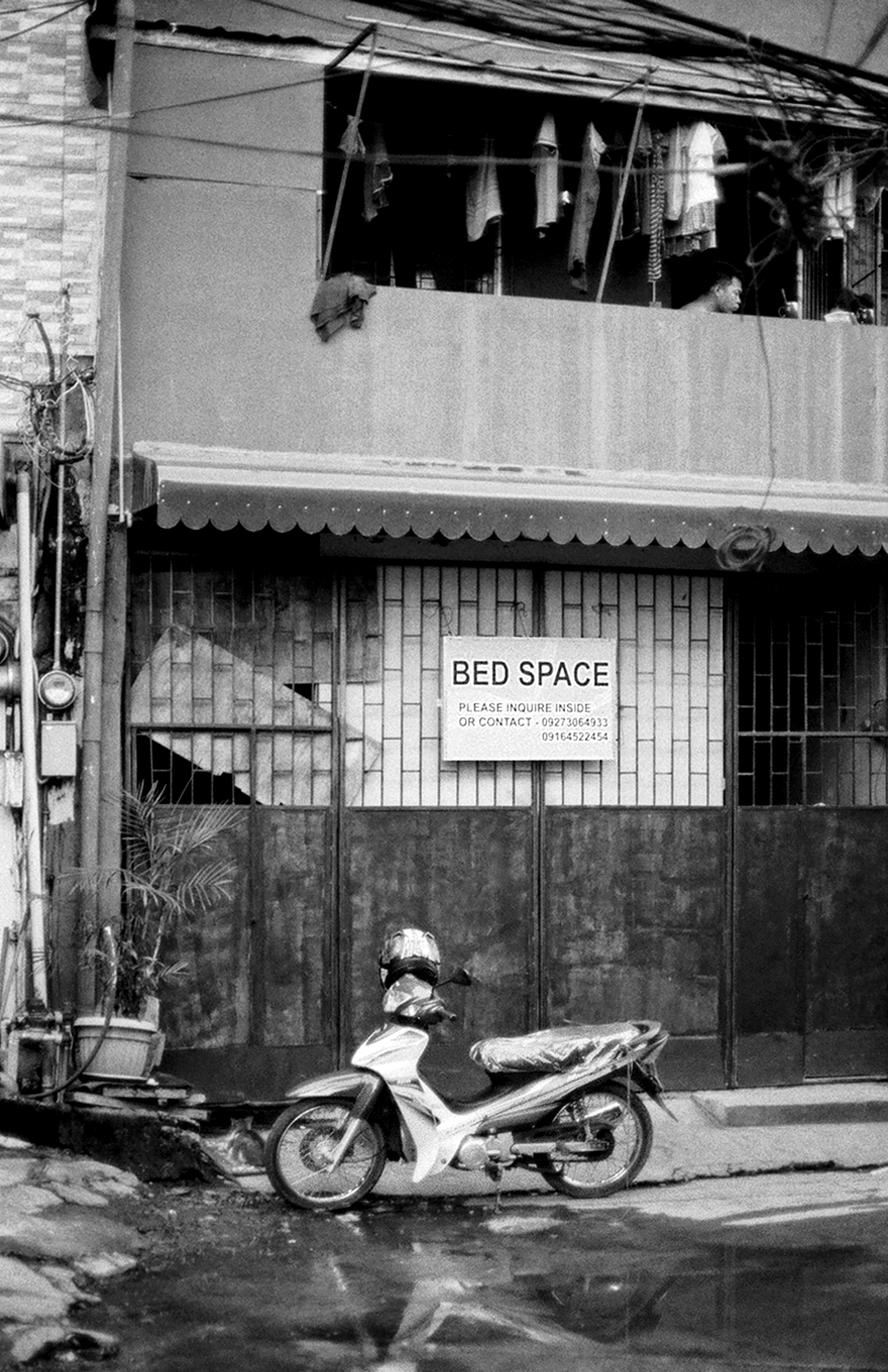 Street scene with Bed Space storefront sign motorcycle parked outside two-story building with corrugated metal siding tangled power lines