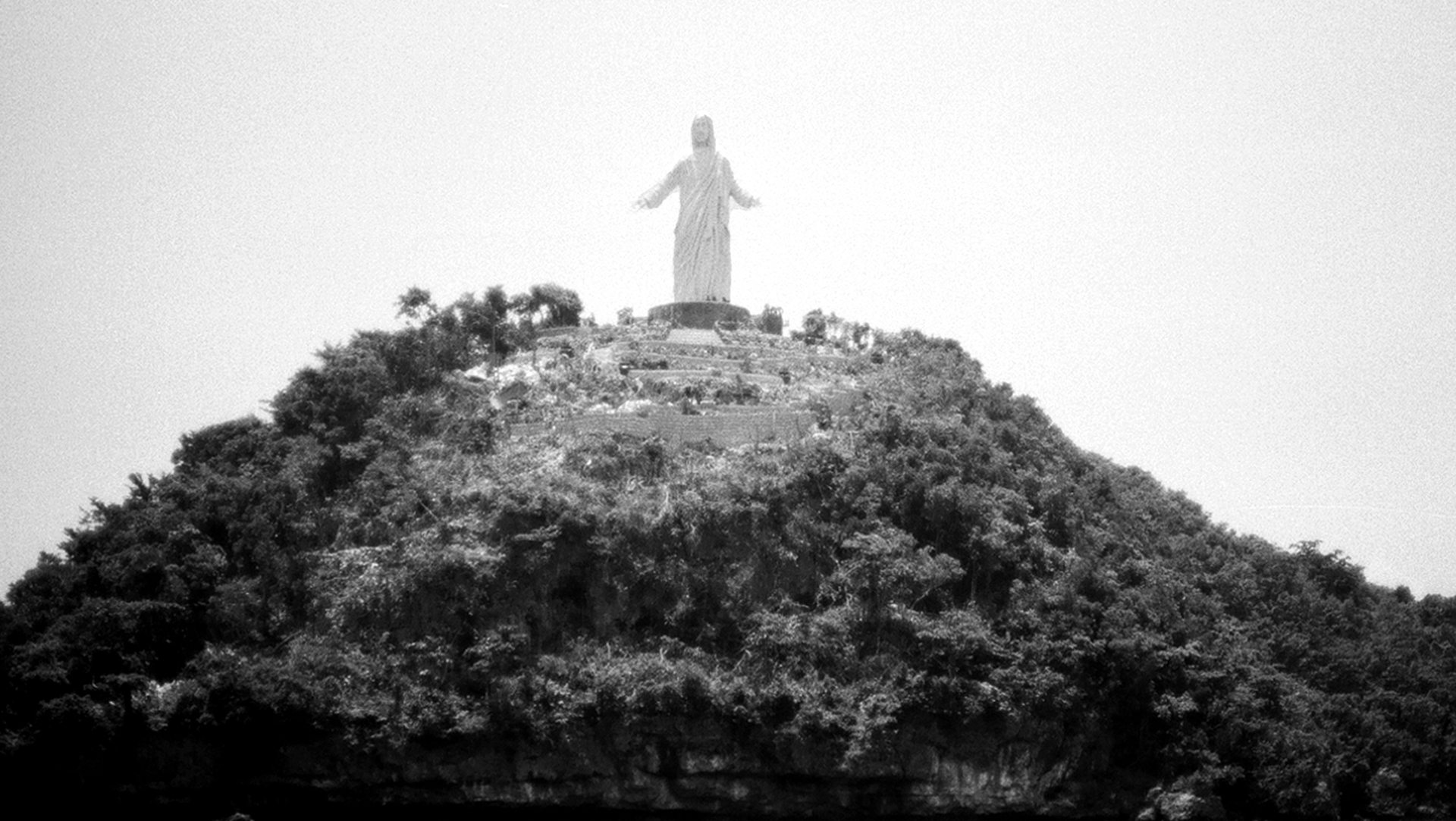 Religious statue on hilltop overlooking misty forested valley landscape