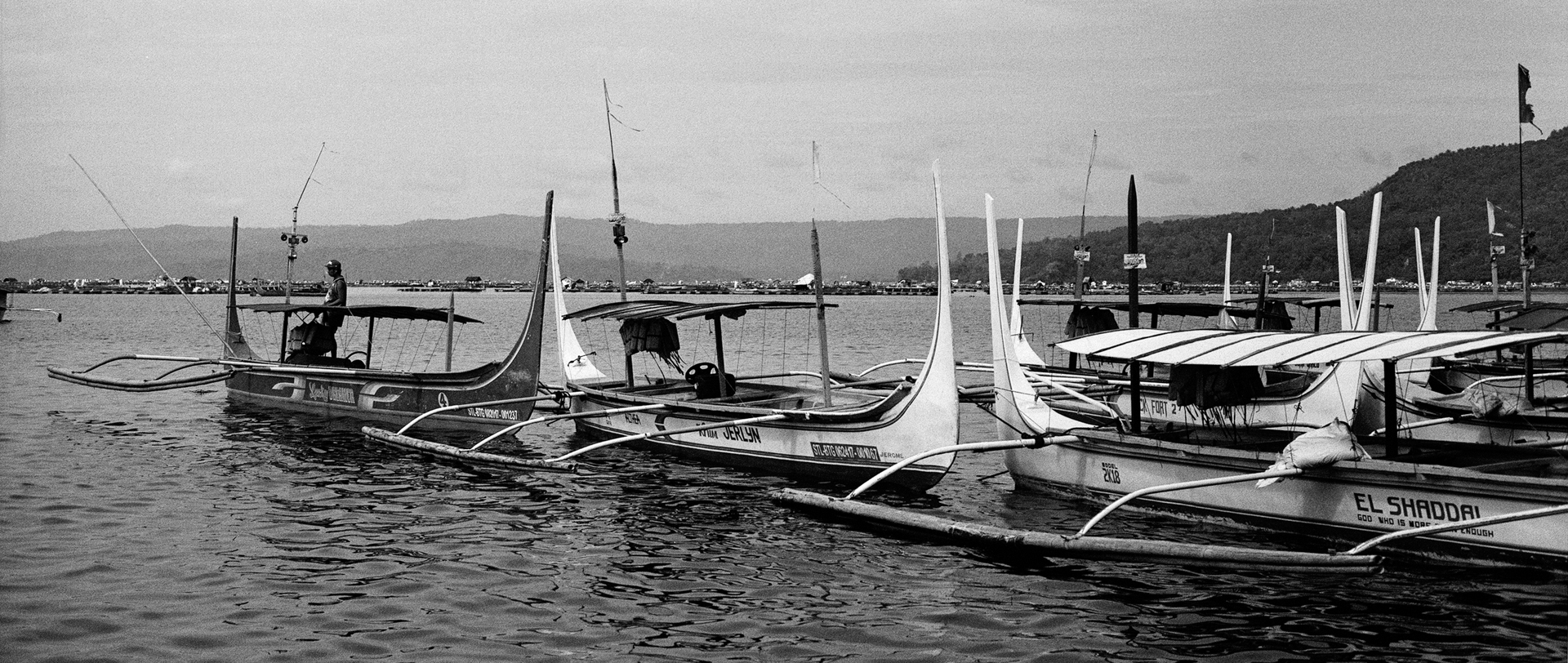 Black and white fishing boats moored in bay with tall sails mountains and distant landscape