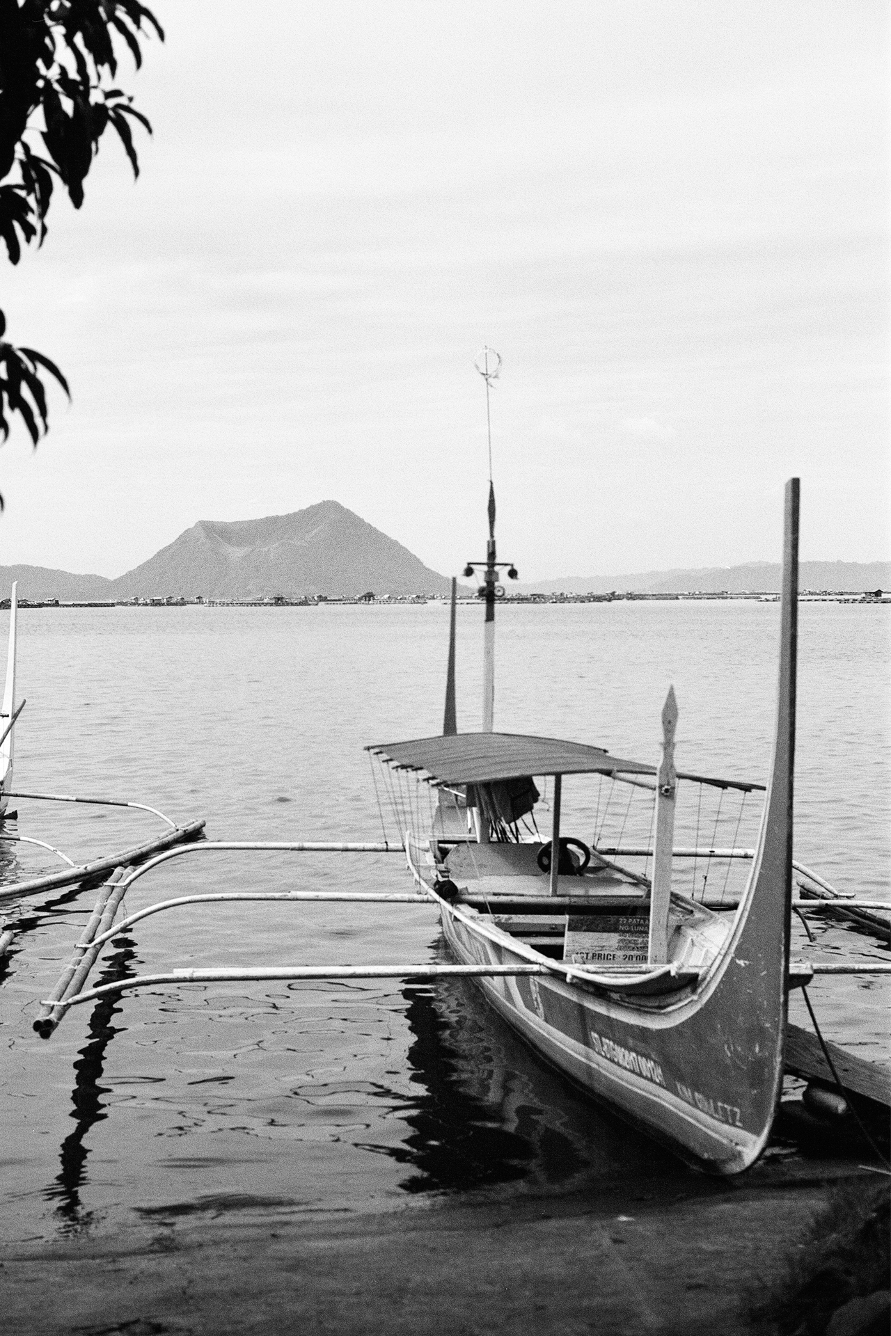 Black and white traditional boats in shallow water framed by tree branches mountains visible