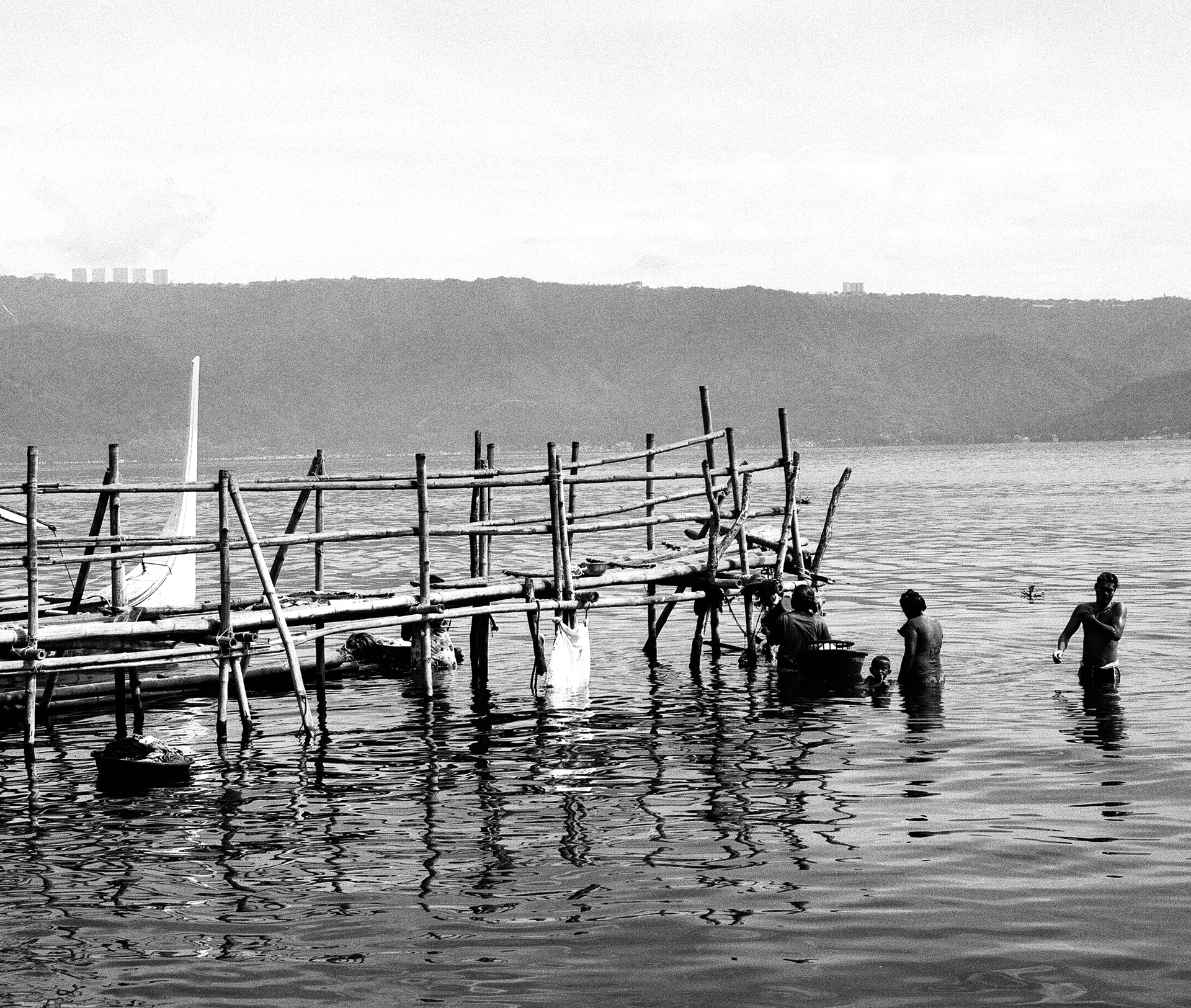 Black and white waterfront dock with wooden pier structure people wading in calm water bay